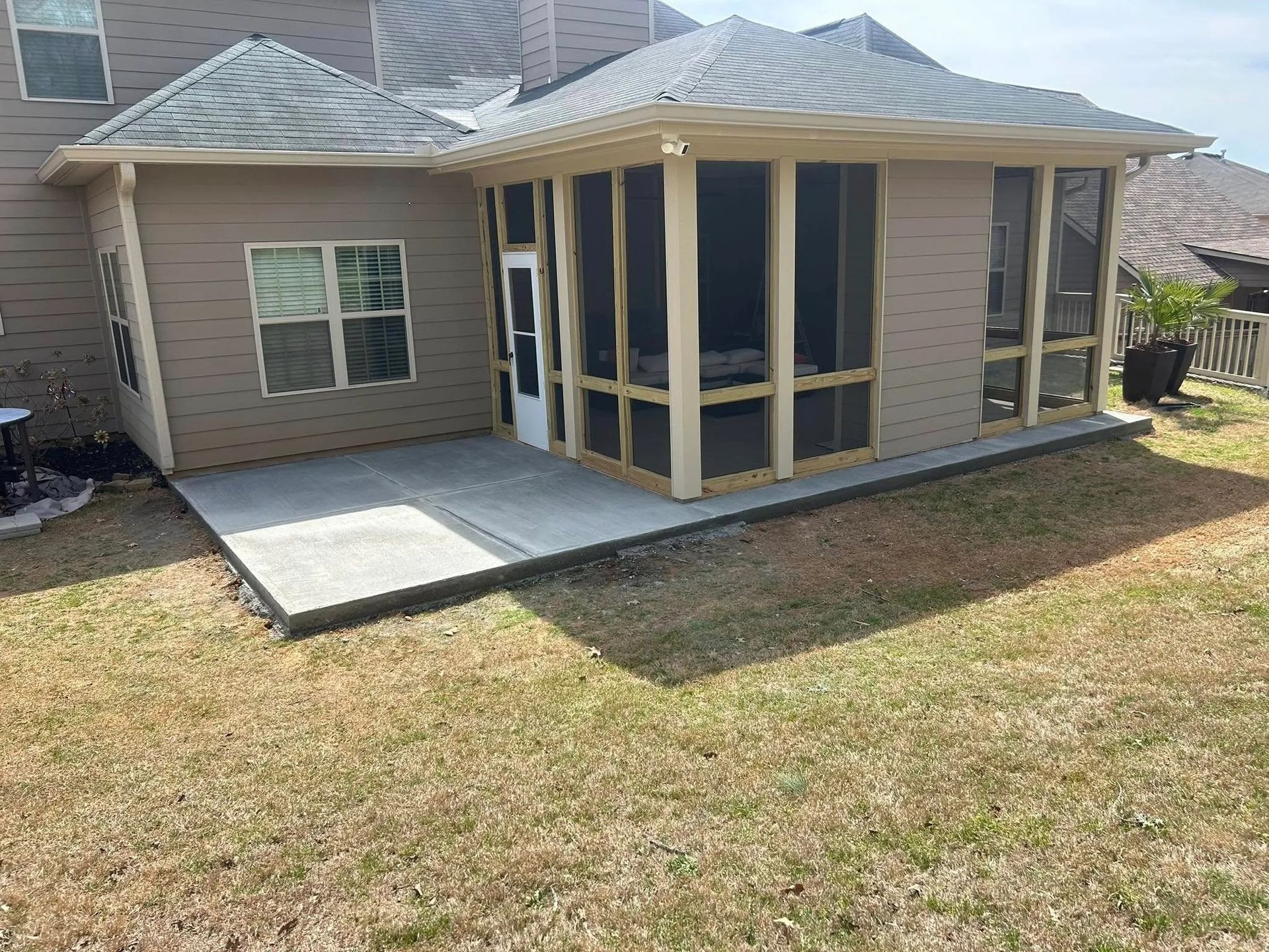Backyard view of a house with a screened porch, concrete patio, and dry grass lawn