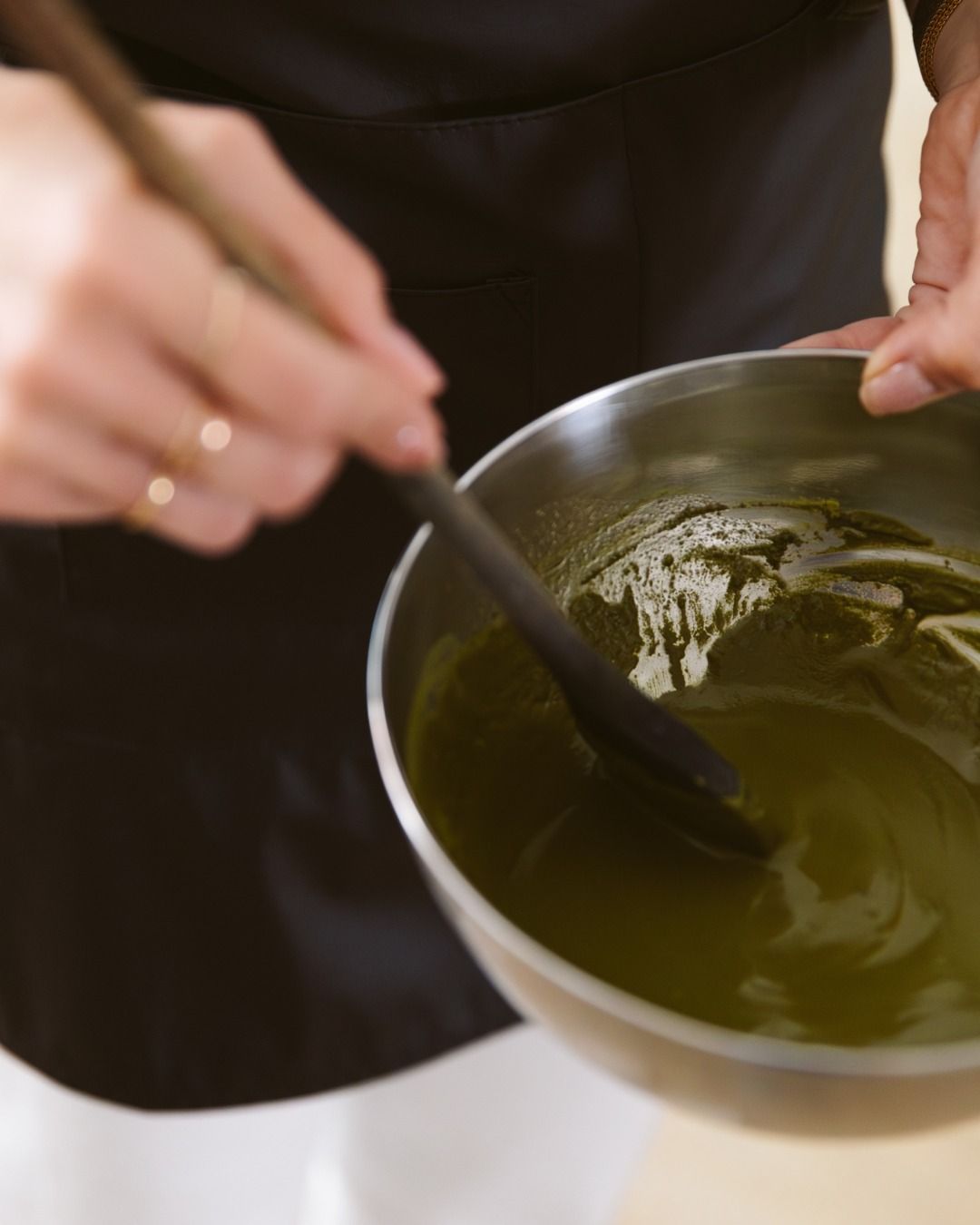 Une personne remue un bol de liquide vert avec une cuillère en bois