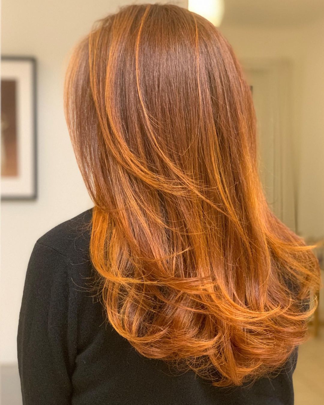 Une femme aux longs cheveux roux porte un pull noir.