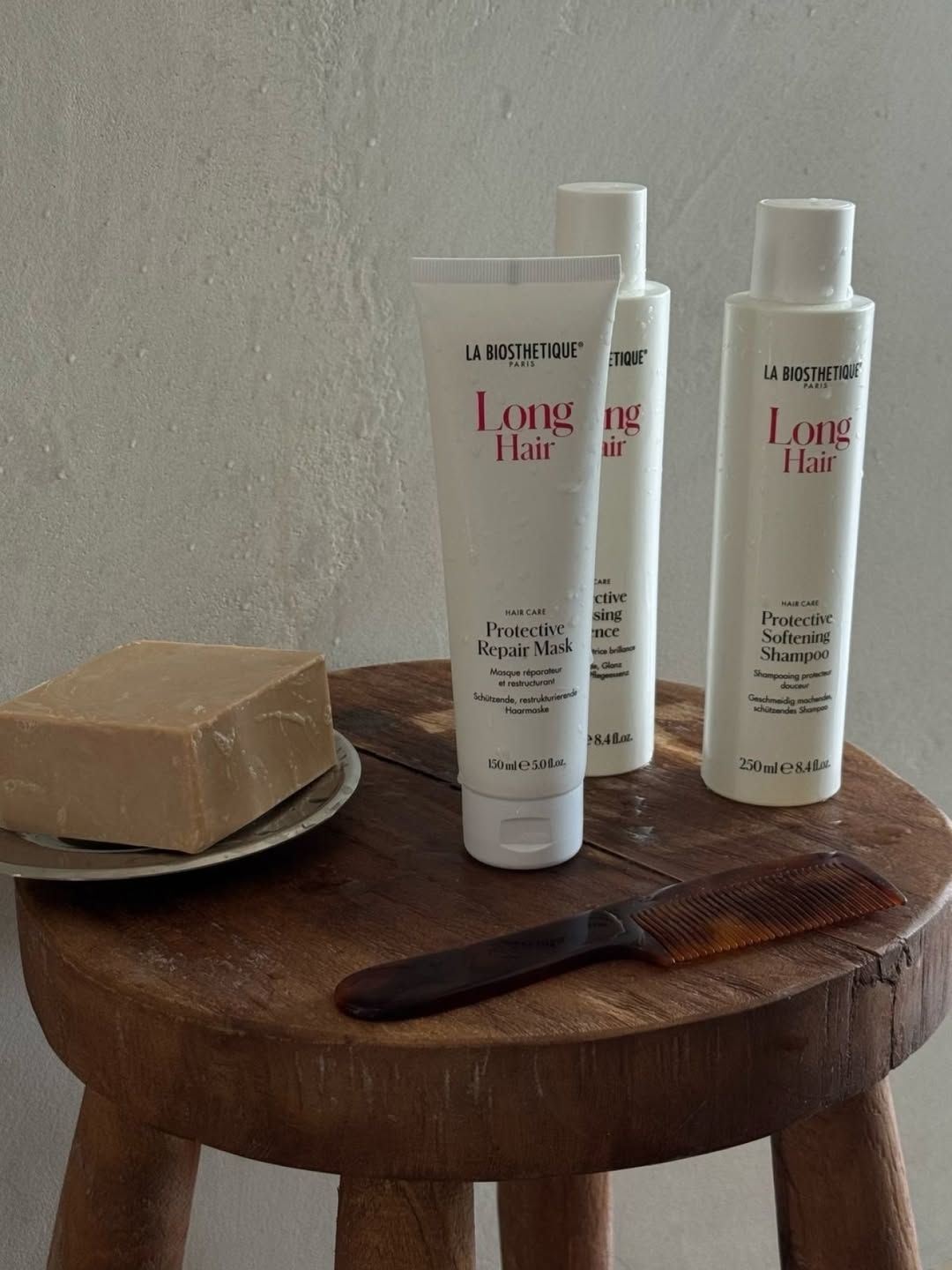 Trois bouteilles de produits pour cheveux longs sont sur un tabouret en bois