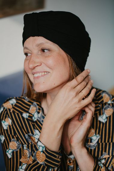 Une femme portant un chapeau noir et une chemise rayée sourit.