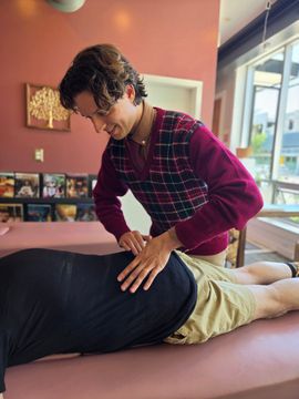 Therapist pressing a client’s back on a massage table in a pink treatment room