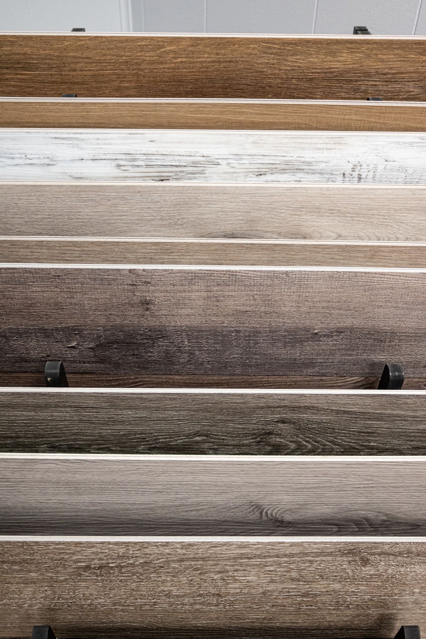 Wooden flooring samples in various shades of brown and gray, displayed on a rack.