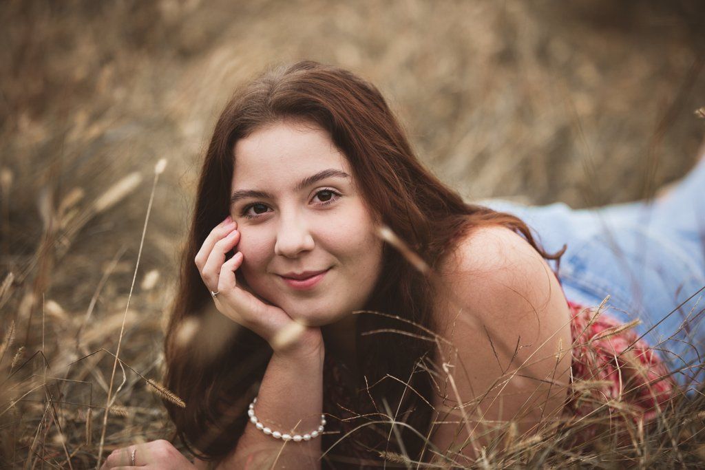 A young woman is laying in the grass with her hand on her face.
