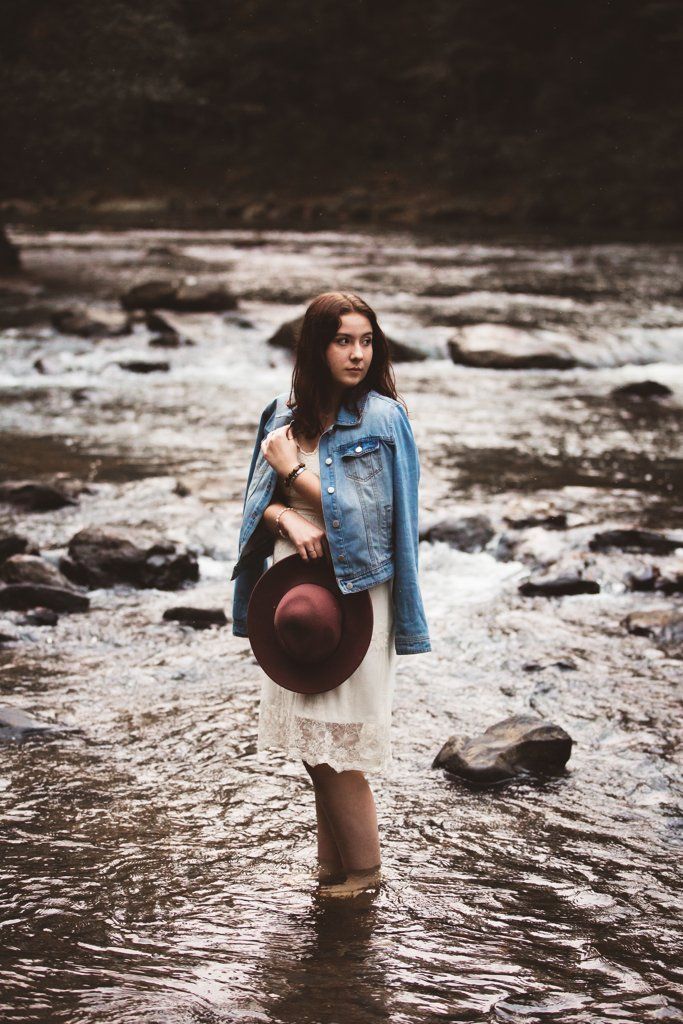 A woman is standing in a river holding a hat.