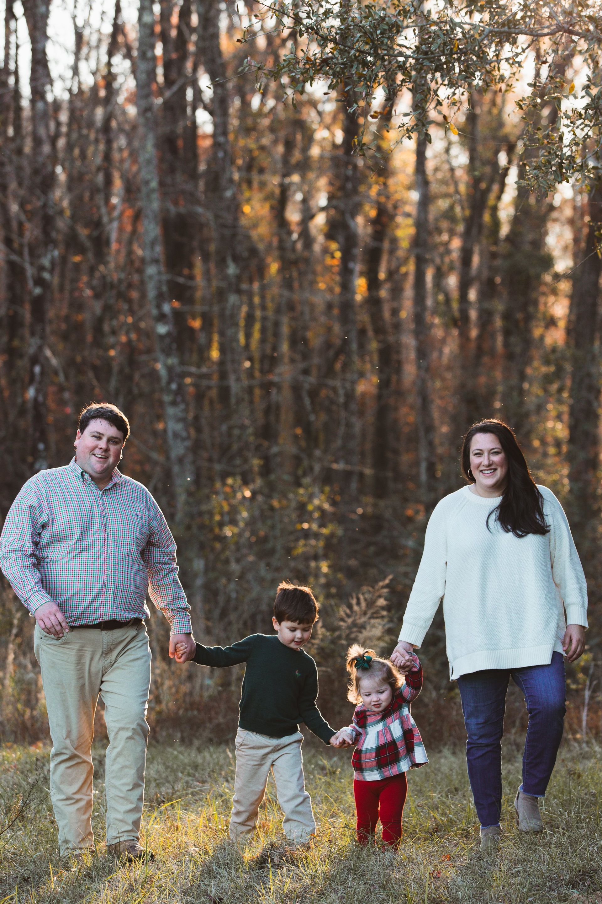 A family is walking through the woods holding hands.
