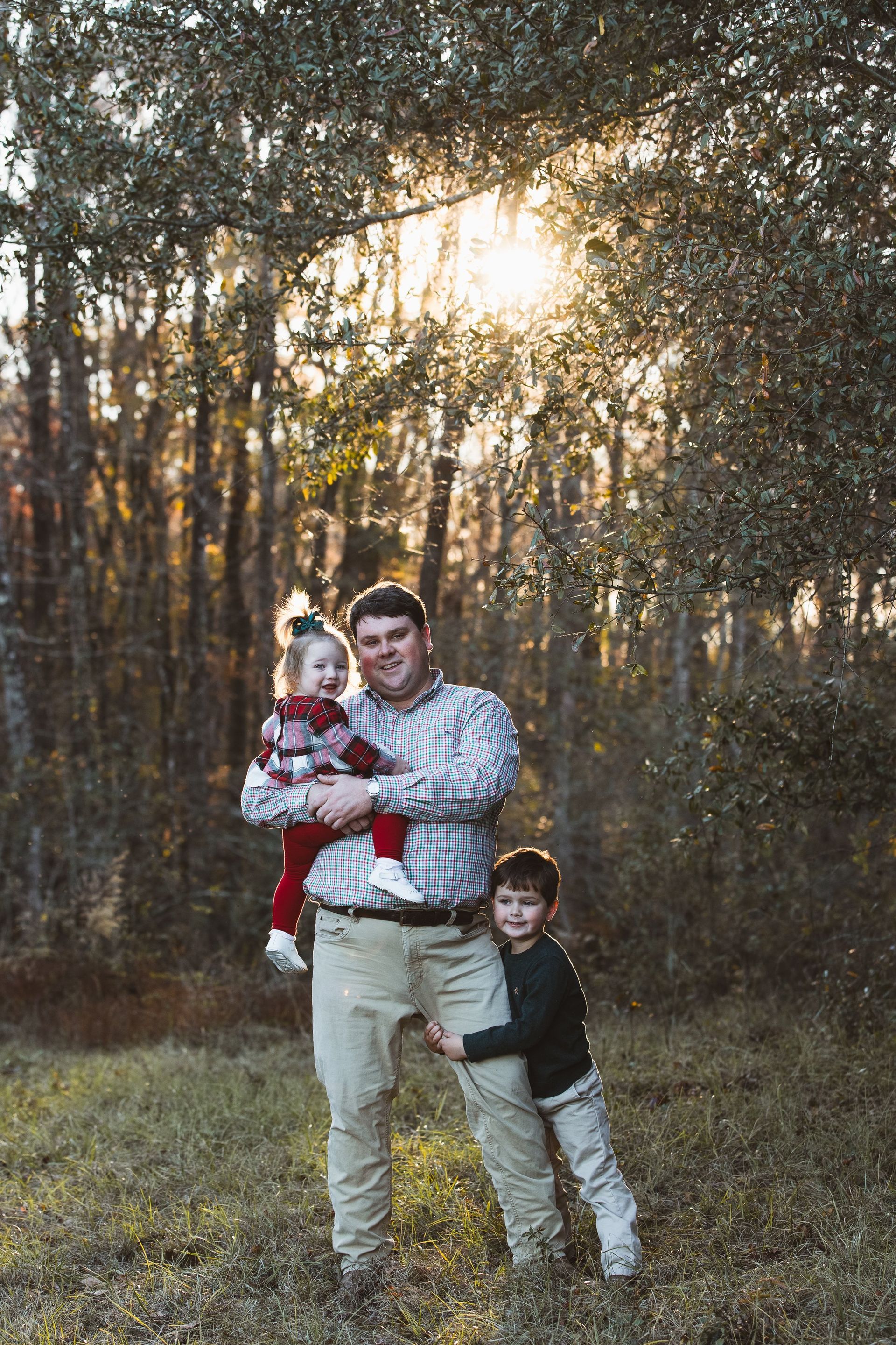 A man is holding a baby and two children in a field.