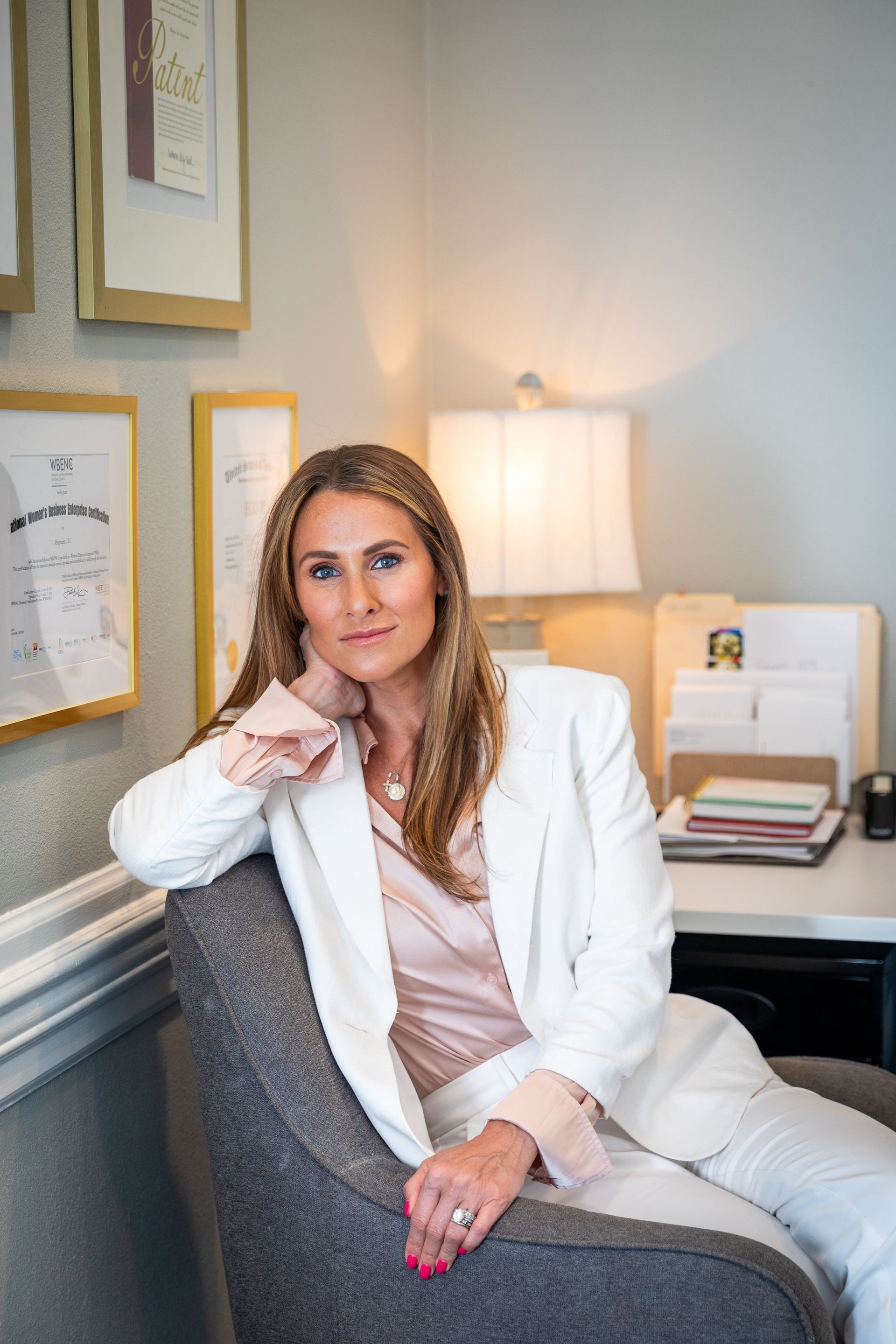 A woman in a white suit is sitting in a chair in front of a desk.