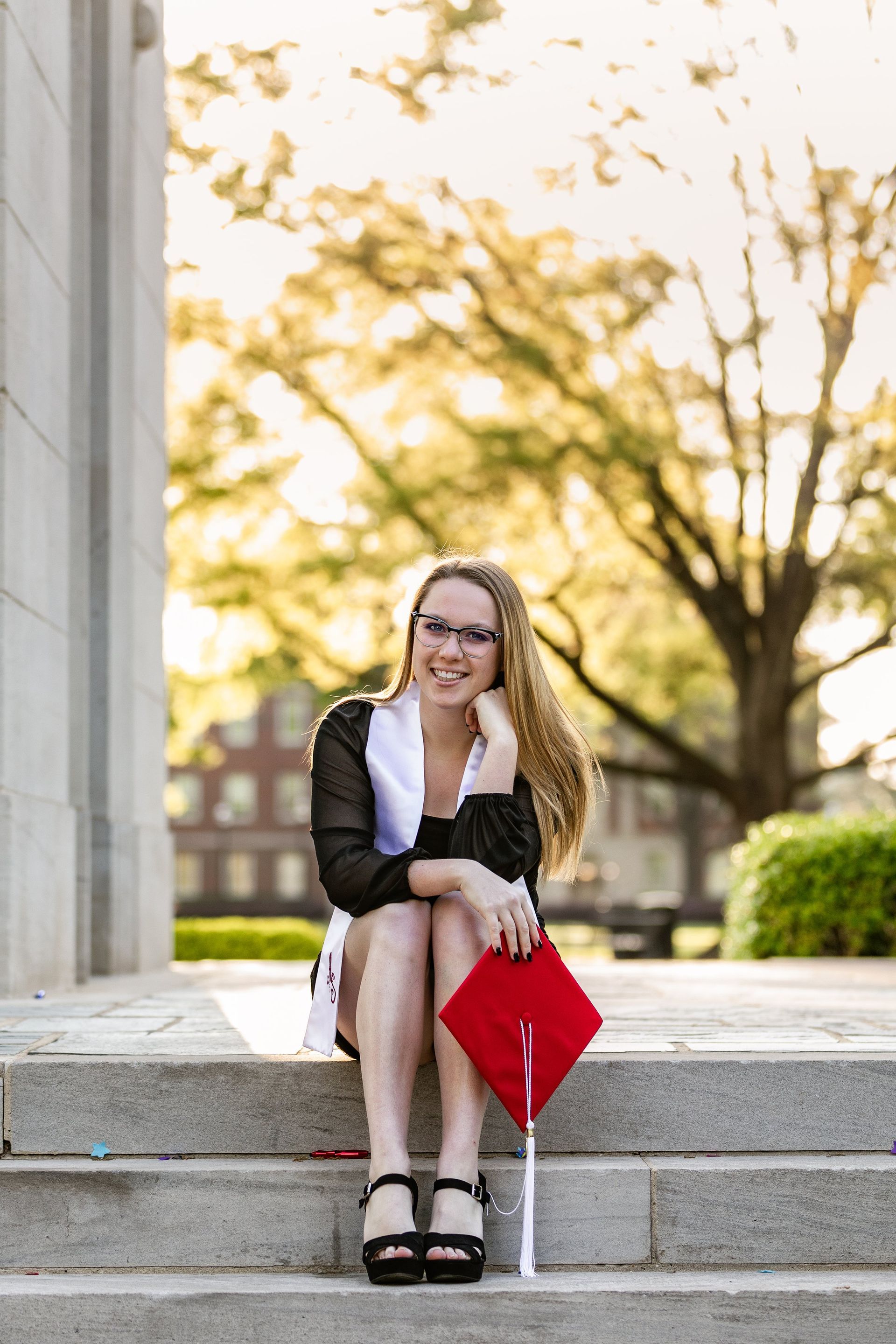 A woman in a graduation cap and gown is sitting on the steps of a building.