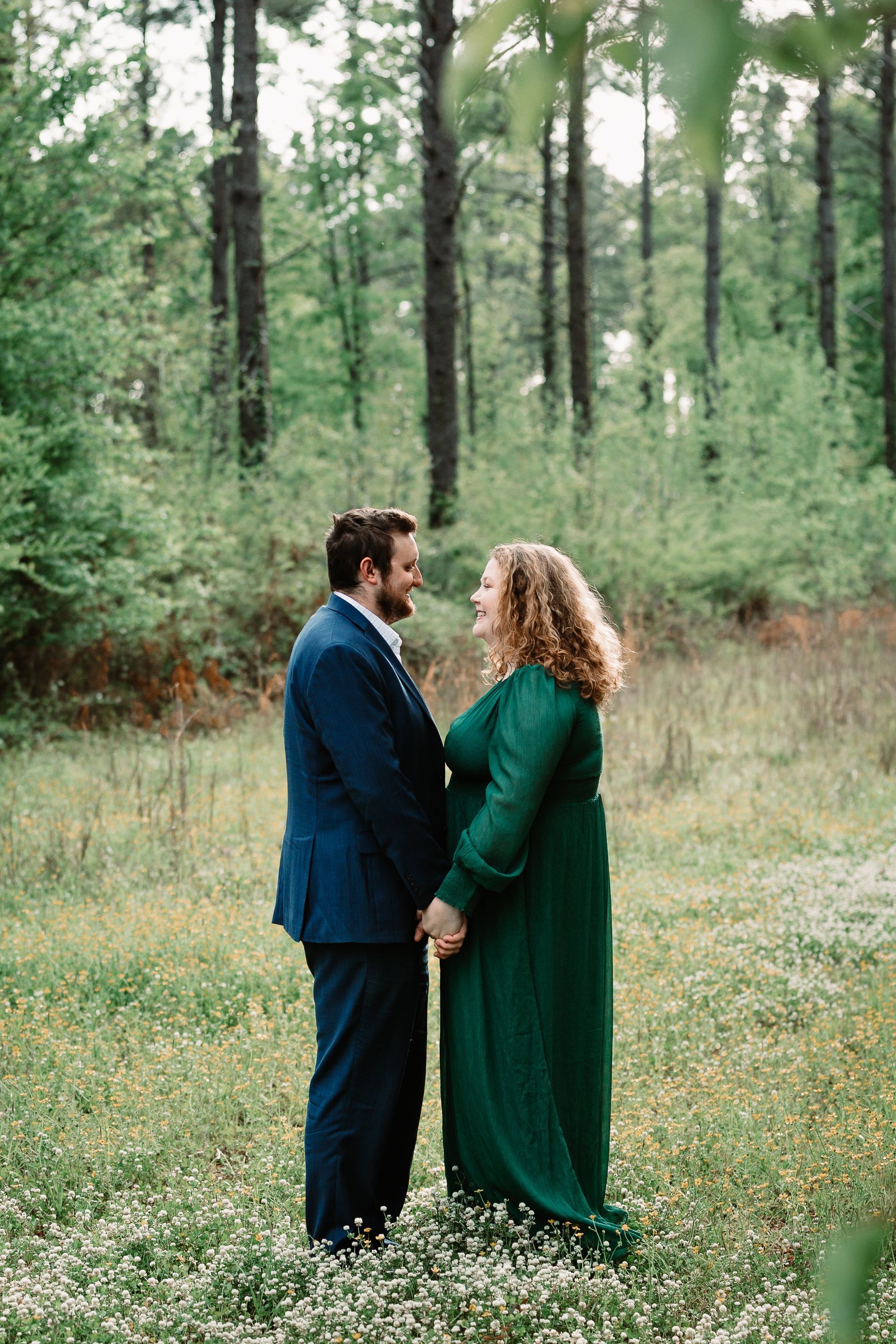 A man and a woman are standing in a field holding hands . the woman is wearing a green dress.