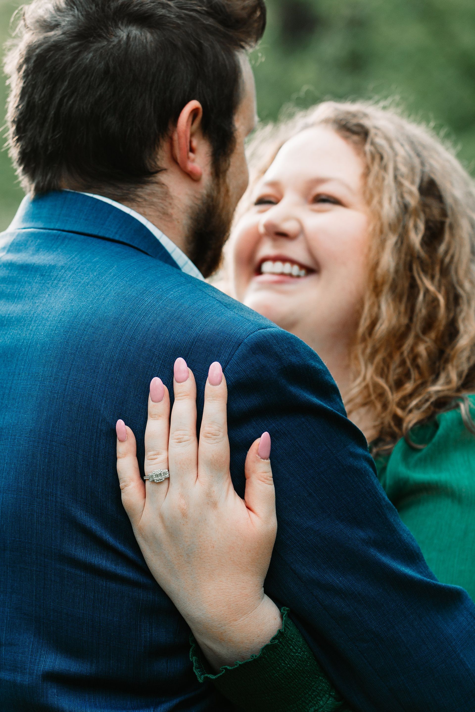 A man and a woman are hugging and the woman is wearing an engagement ring.