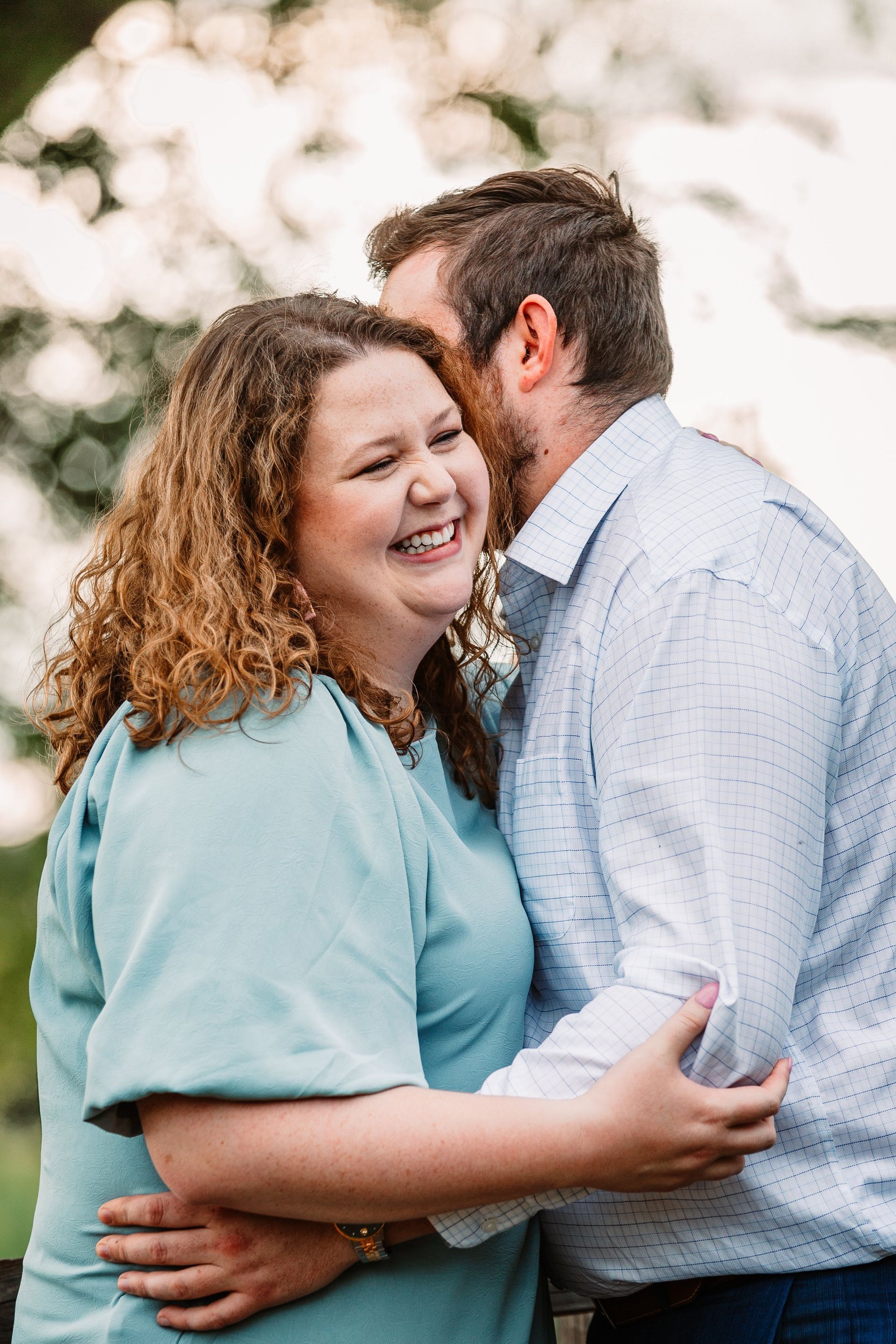 A man is kissing a woman on the cheek while they are hugging and smiling.