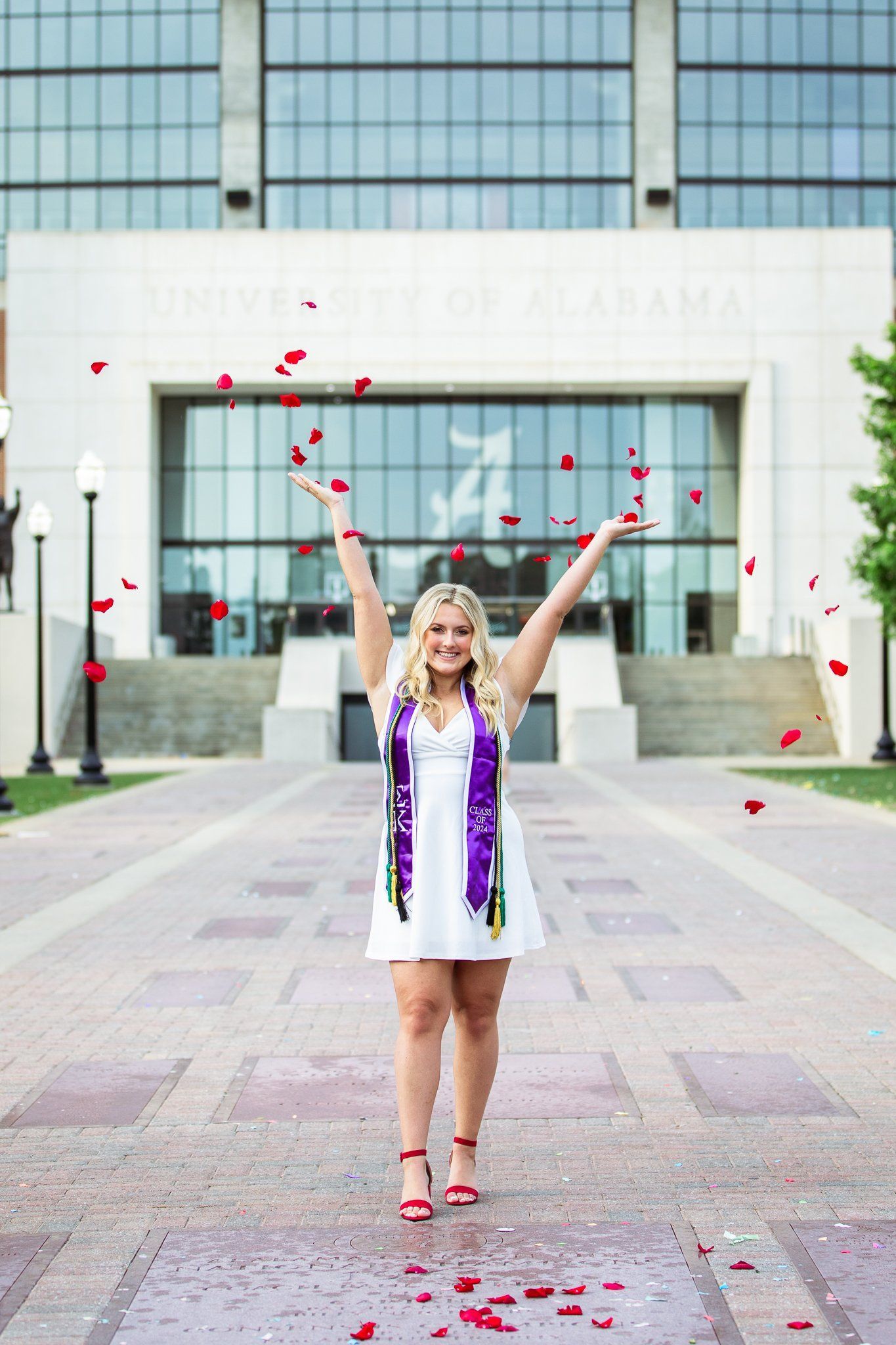 A woman in a white dress and purple scarf is throwing petals in the air.