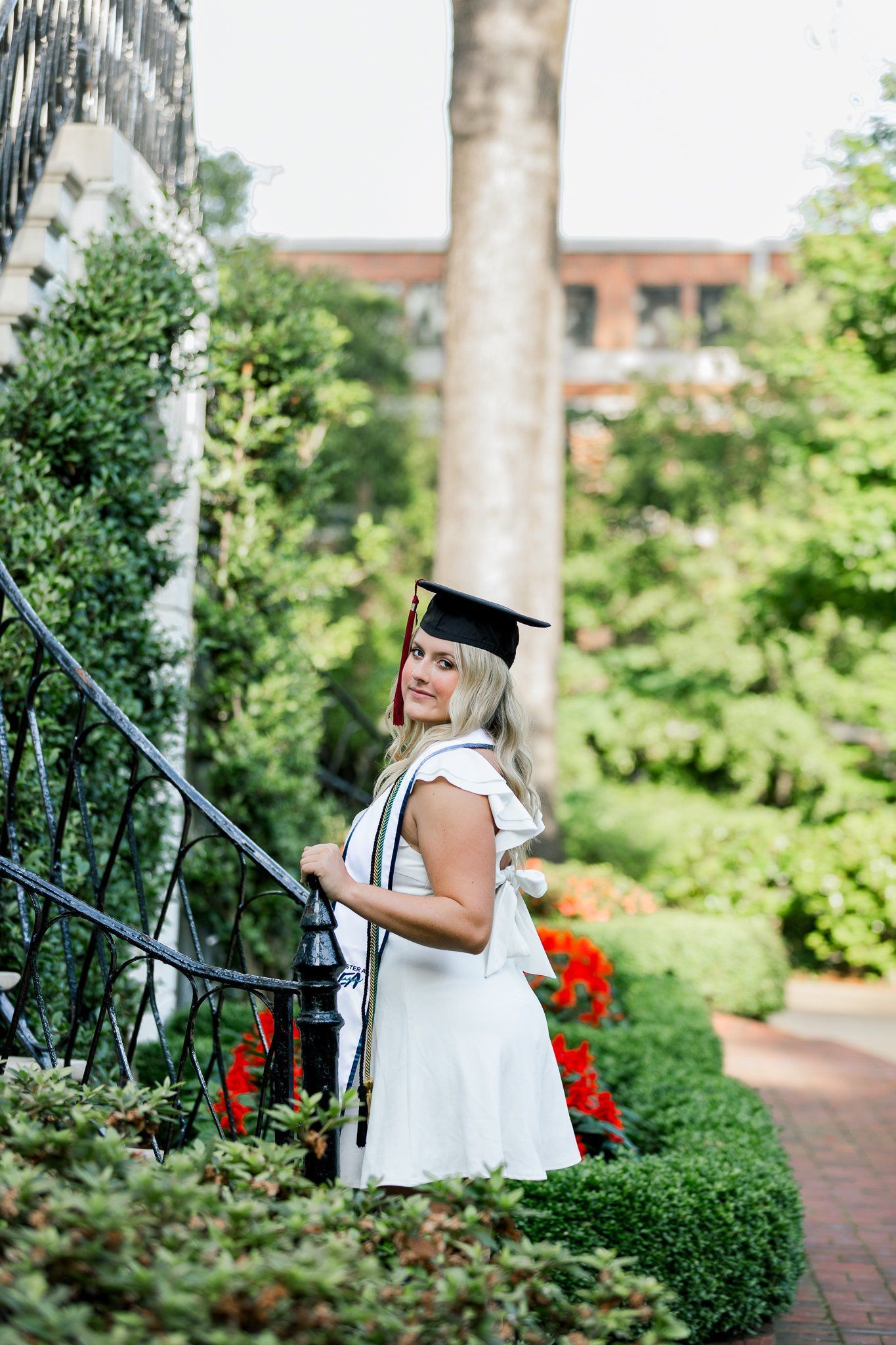 A woman in a graduation cap and gown is standing in a garden.