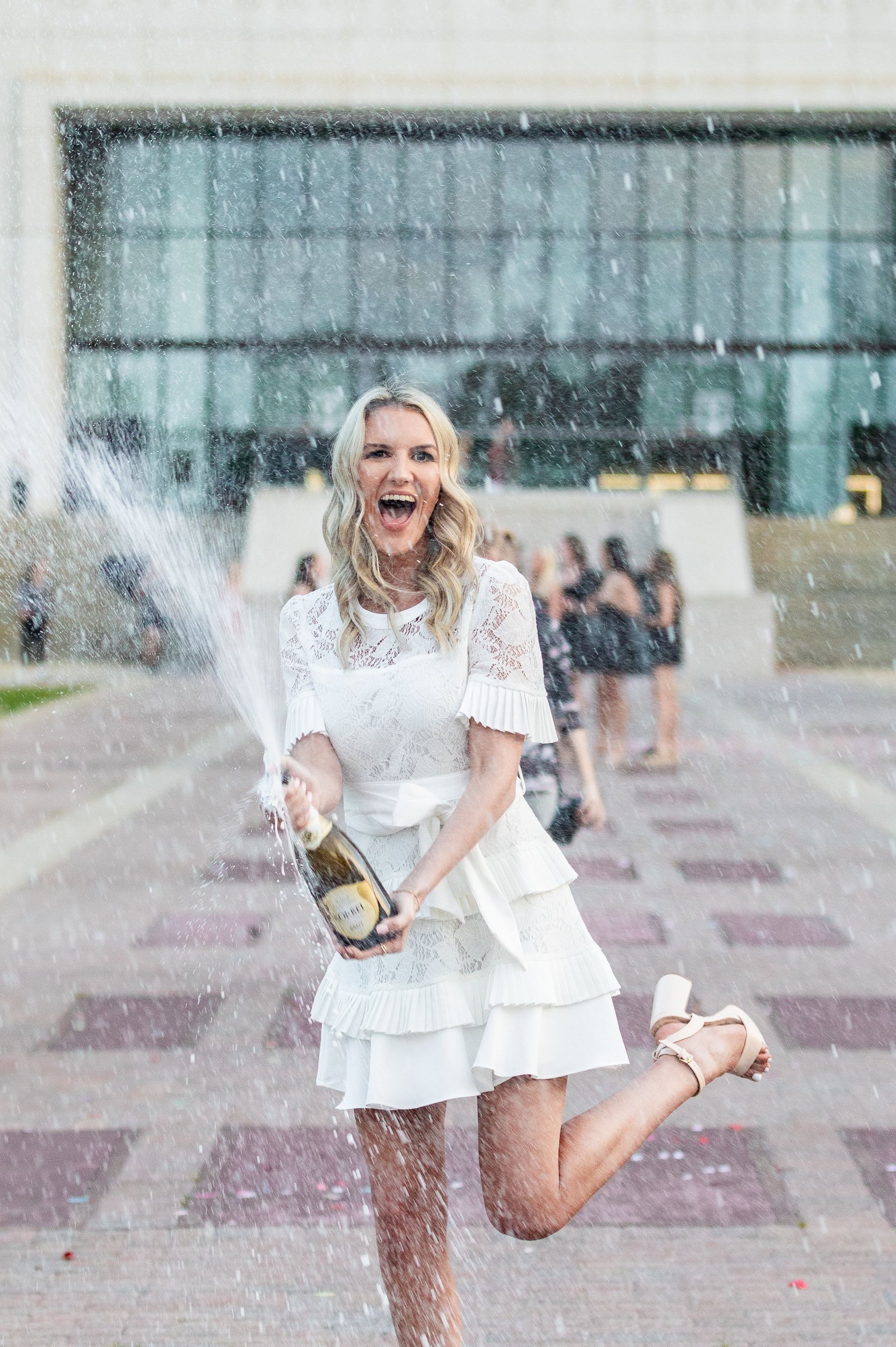 A woman in a white dress is holding a bottle of champagne.