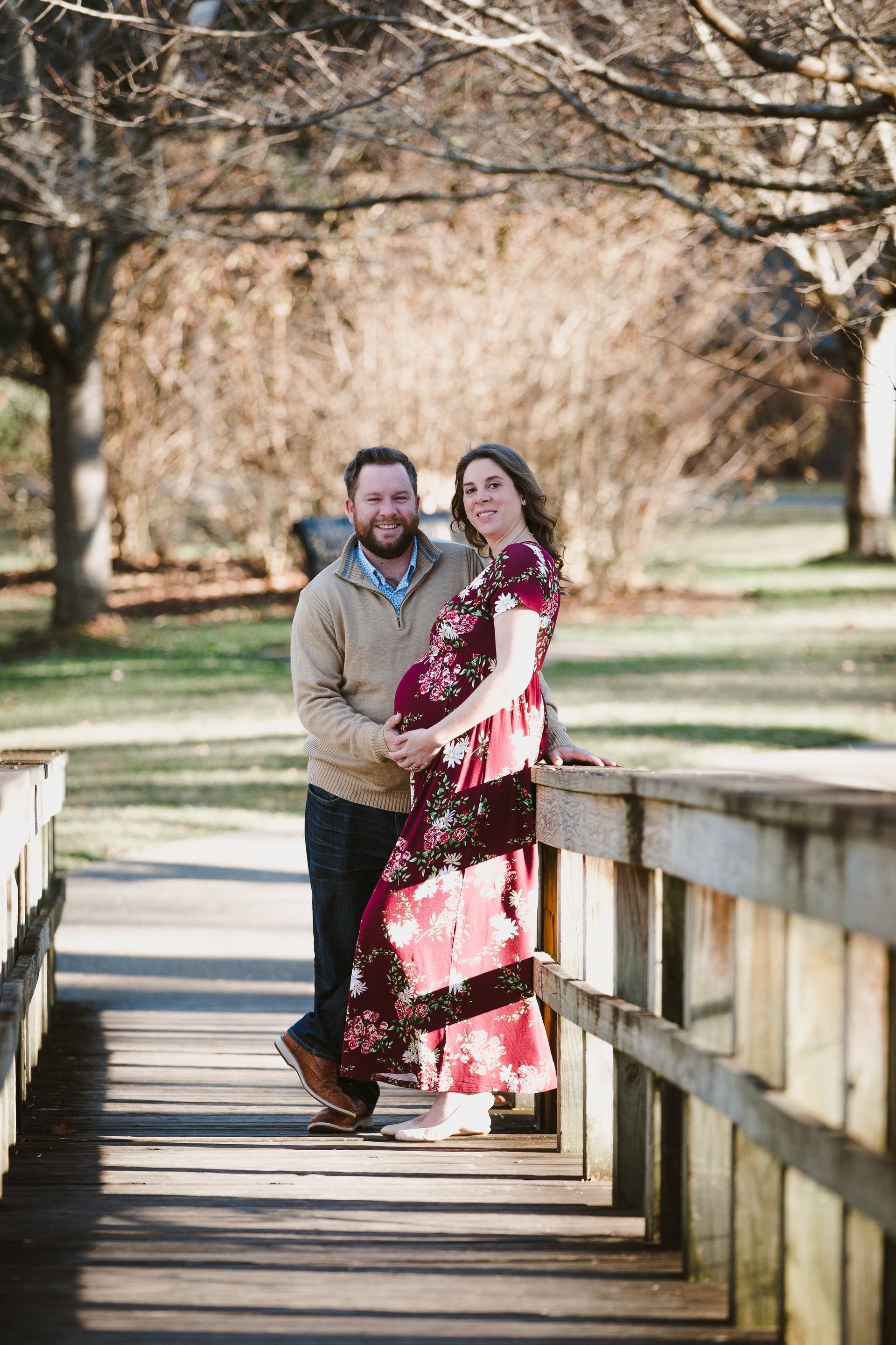 A man and a pregnant woman are standing on a wooden bridge.