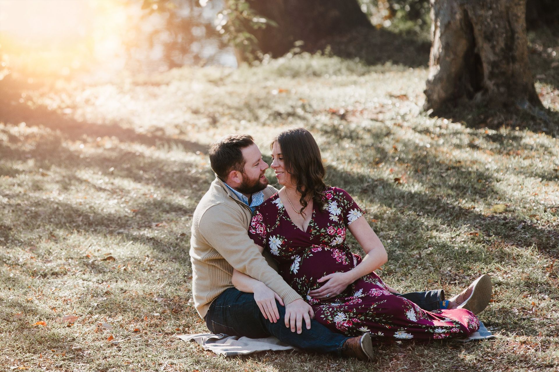A man and a pregnant woman are sitting on a blanket in the grass.