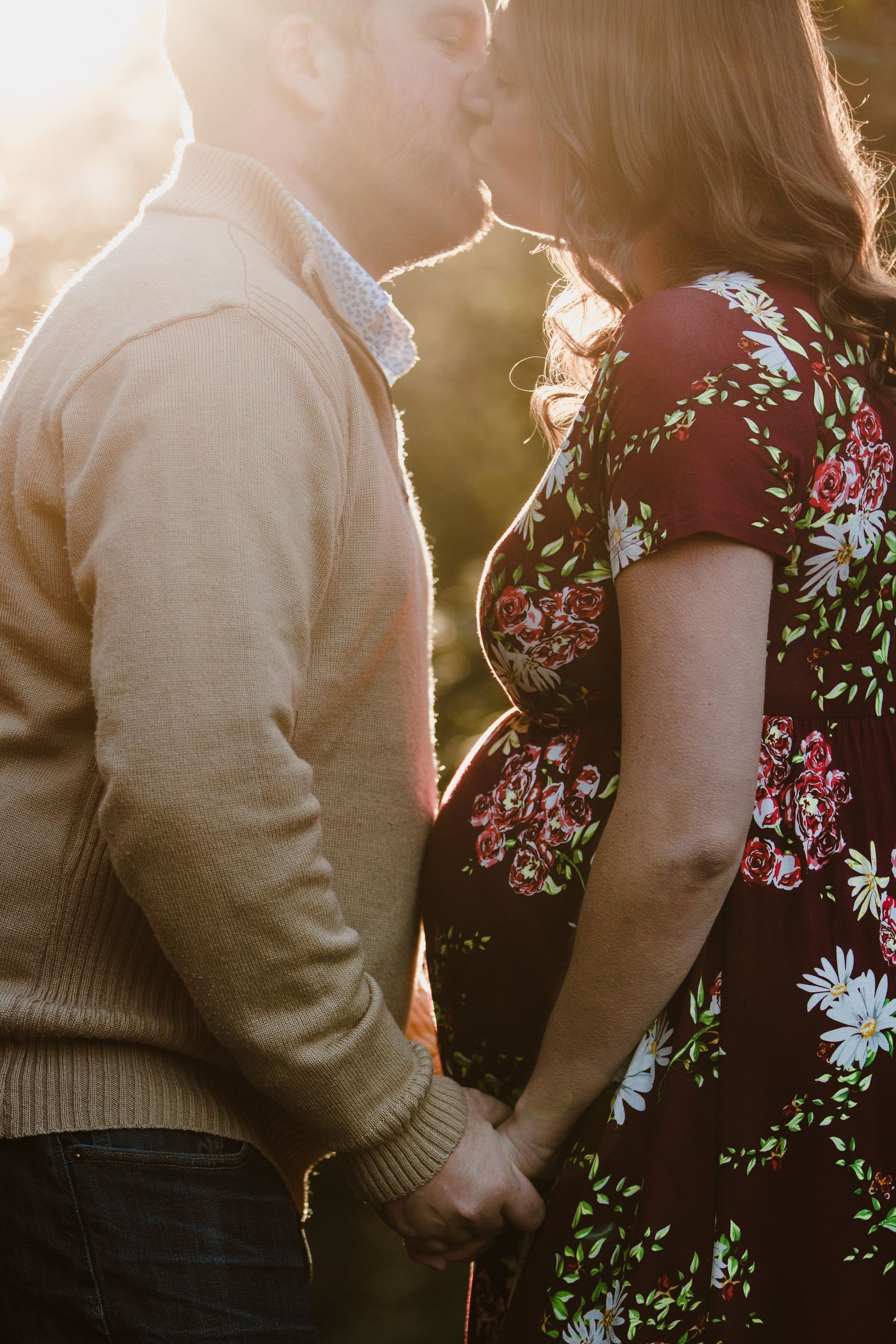 A man and a pregnant woman are kissing while holding hands.