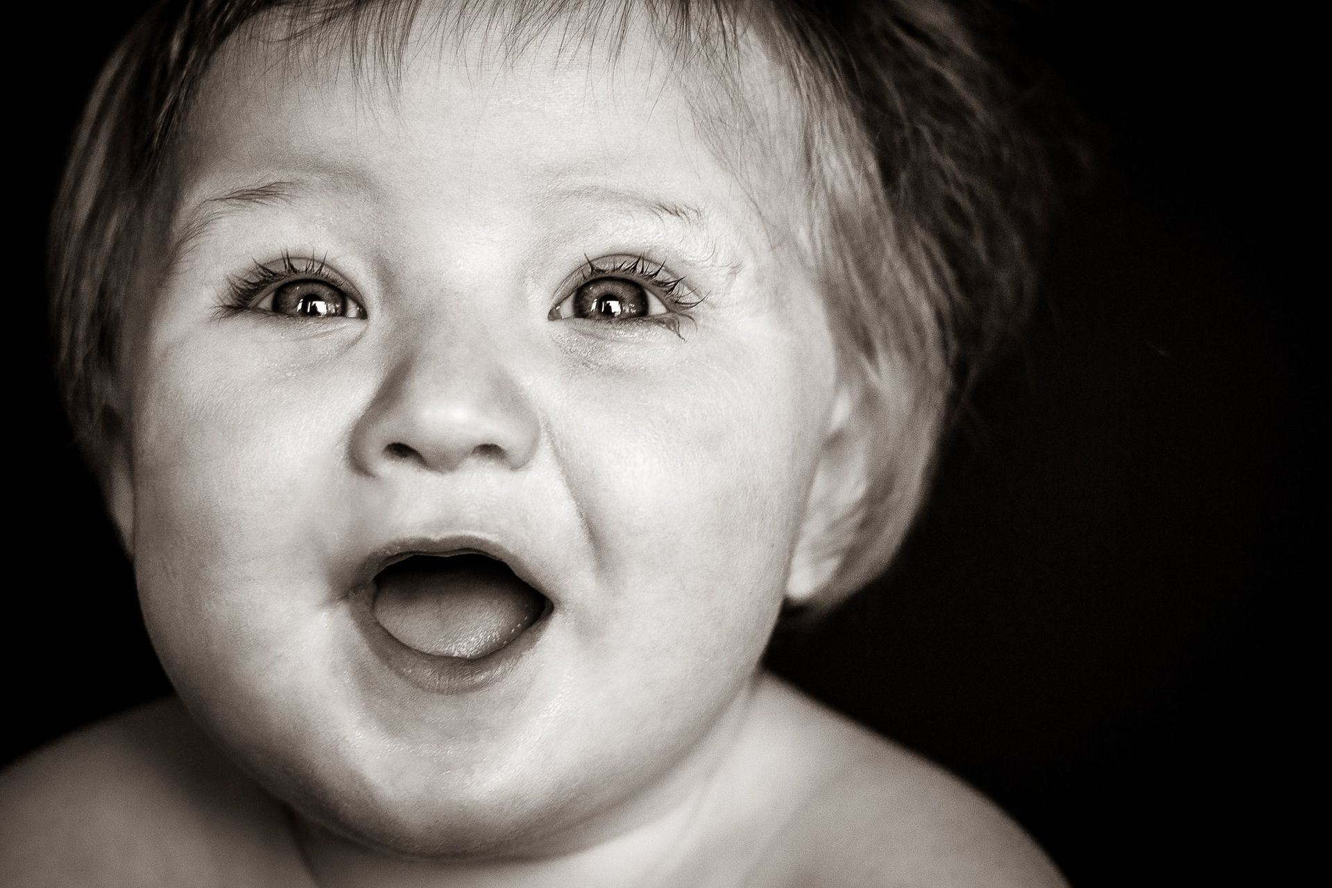 A baby is smiling with his mouth open in a black and white photo.