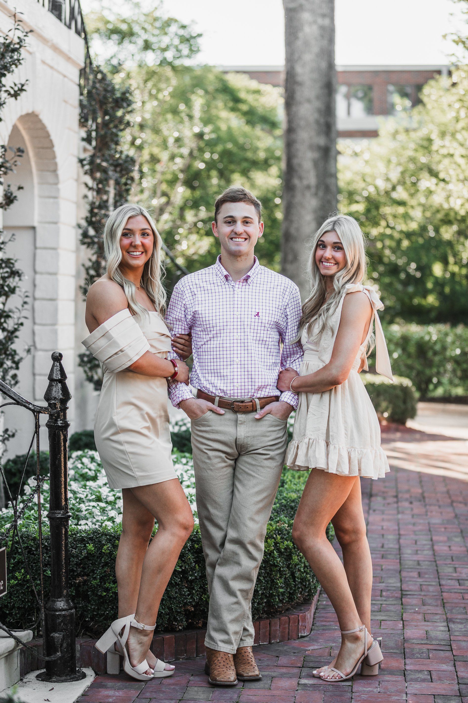 A man and two women are standing next to each other on a brick sidewalk.