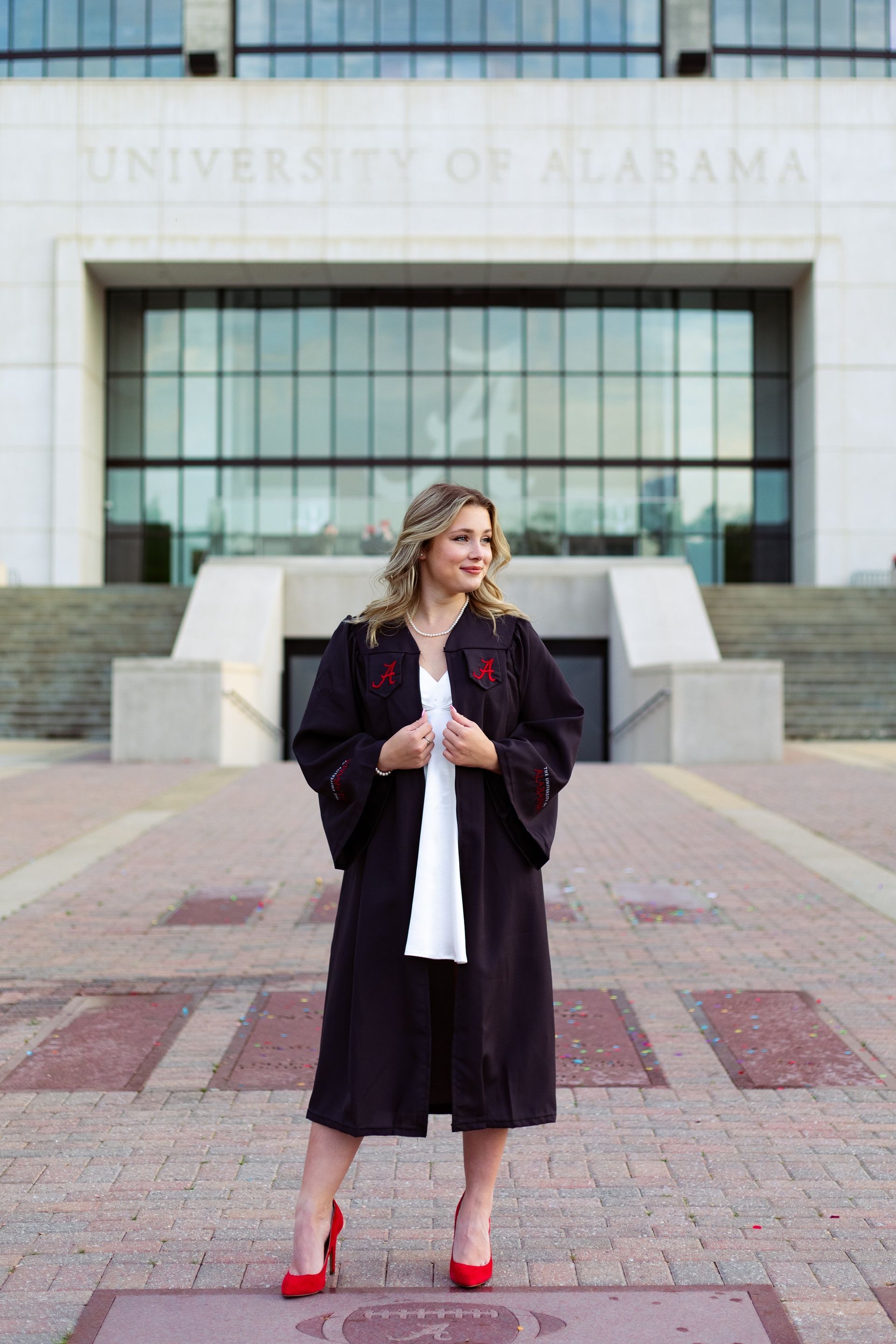 A woman in a graduation cap and gown is standing in front of a building.