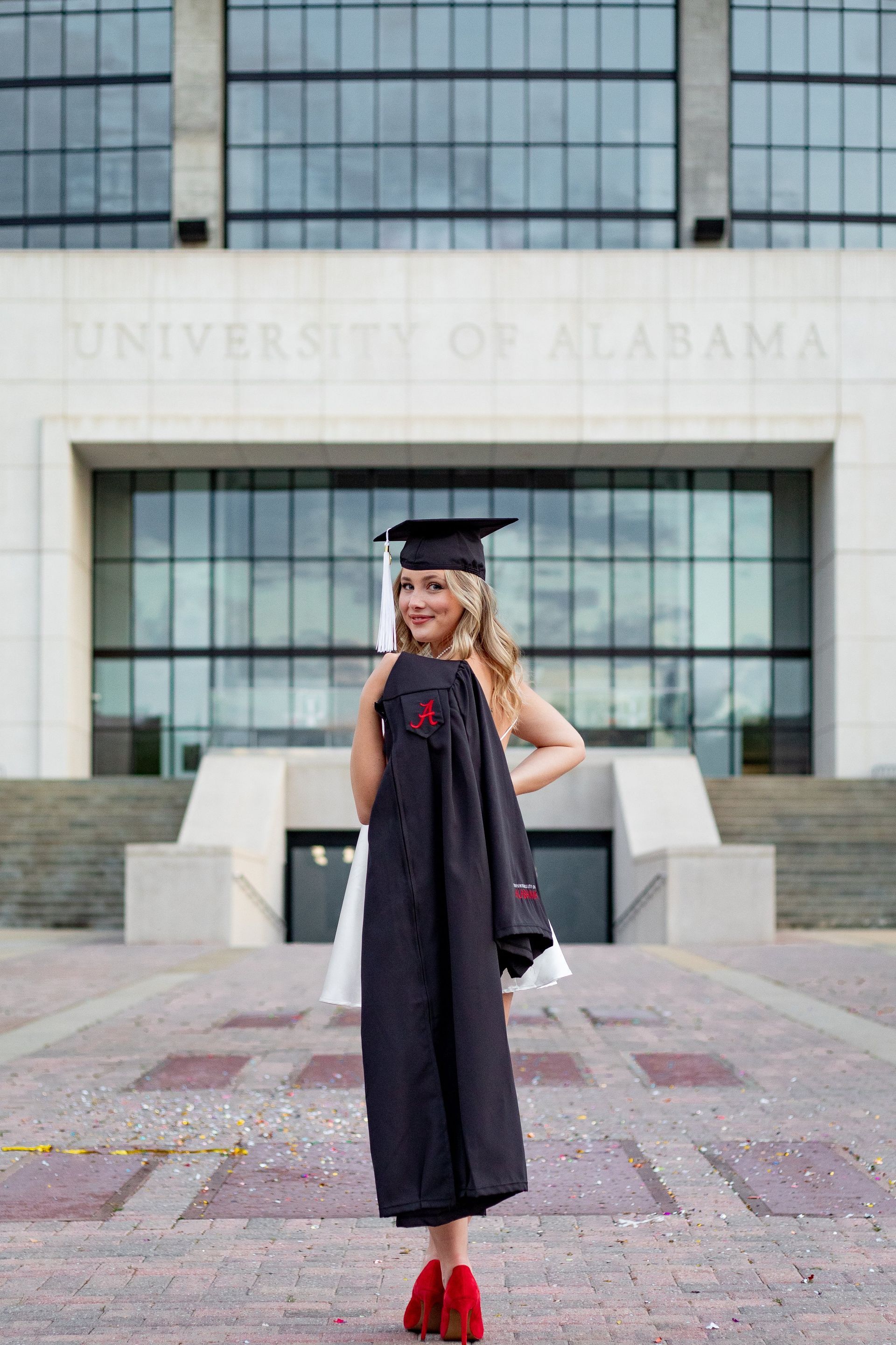 A woman in a graduation cap and gown is standing in front of a building.
