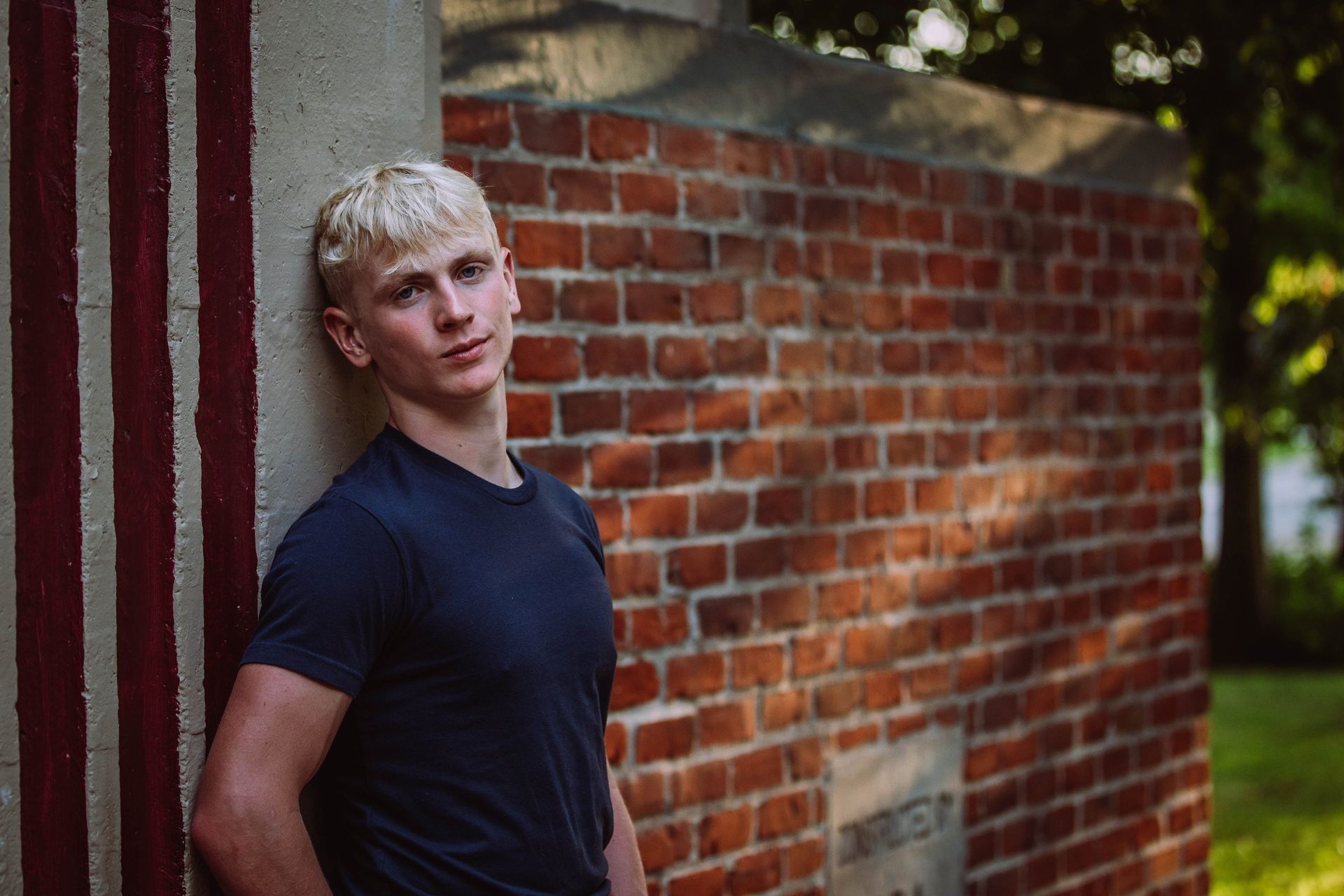 A young man is leaning against a brick wall.