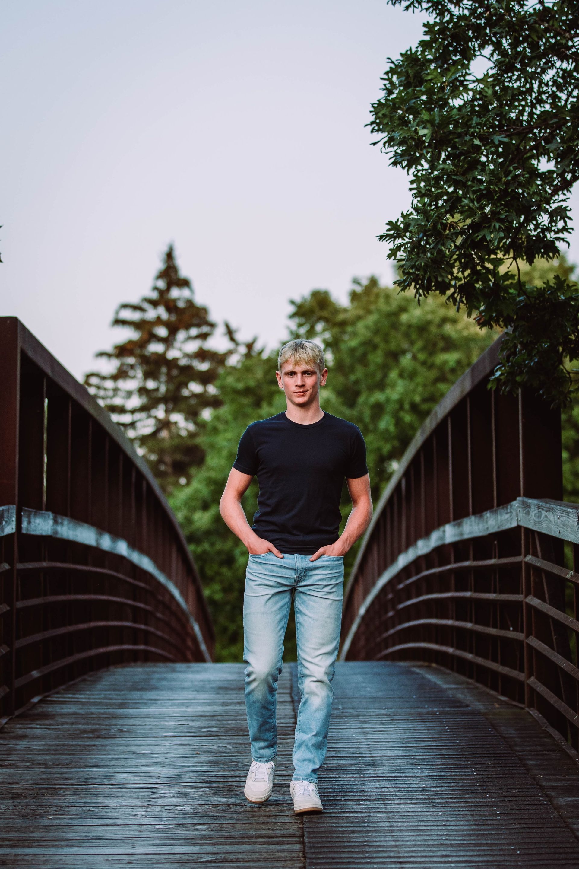 A young man is standing on a bridge with his hands in his pockets.