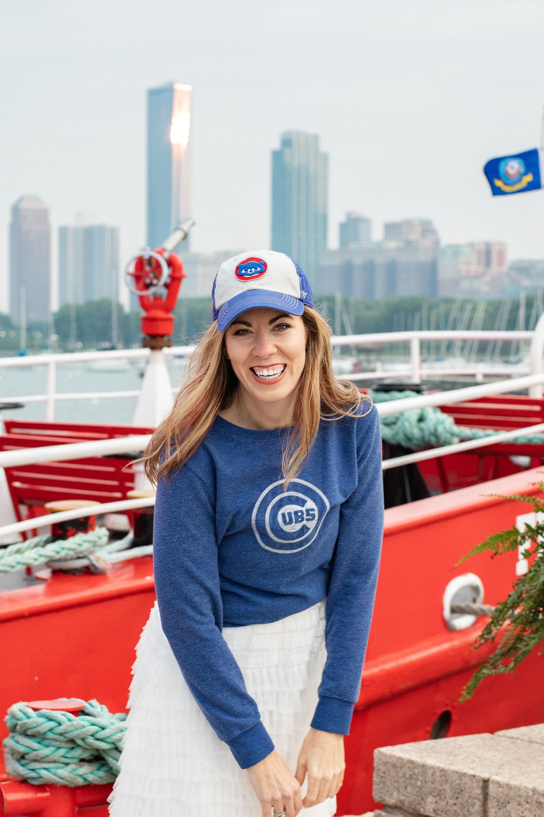 A woman wearing a blue sweater and a hat is standing in front of a red boat.