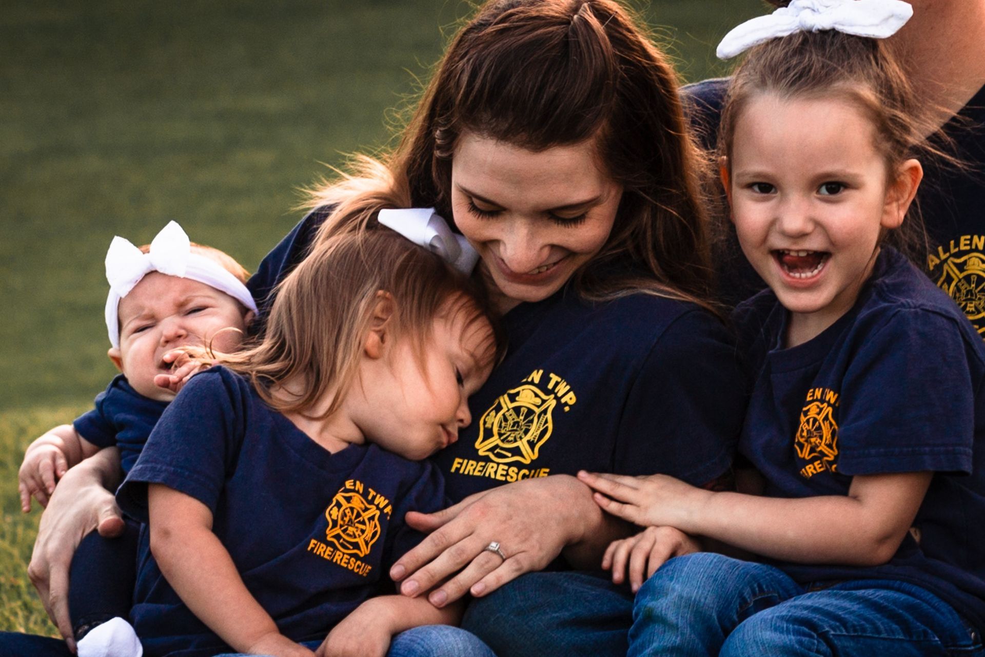 A woman is sitting on the grass with two little girls and a baby.