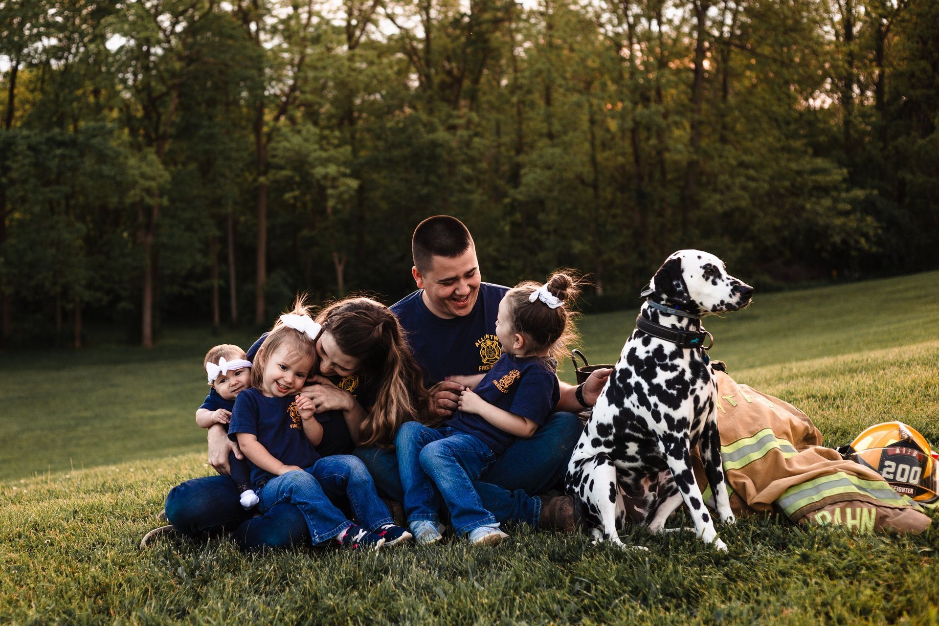 A family is sitting on the grass with a dalmatian dog.