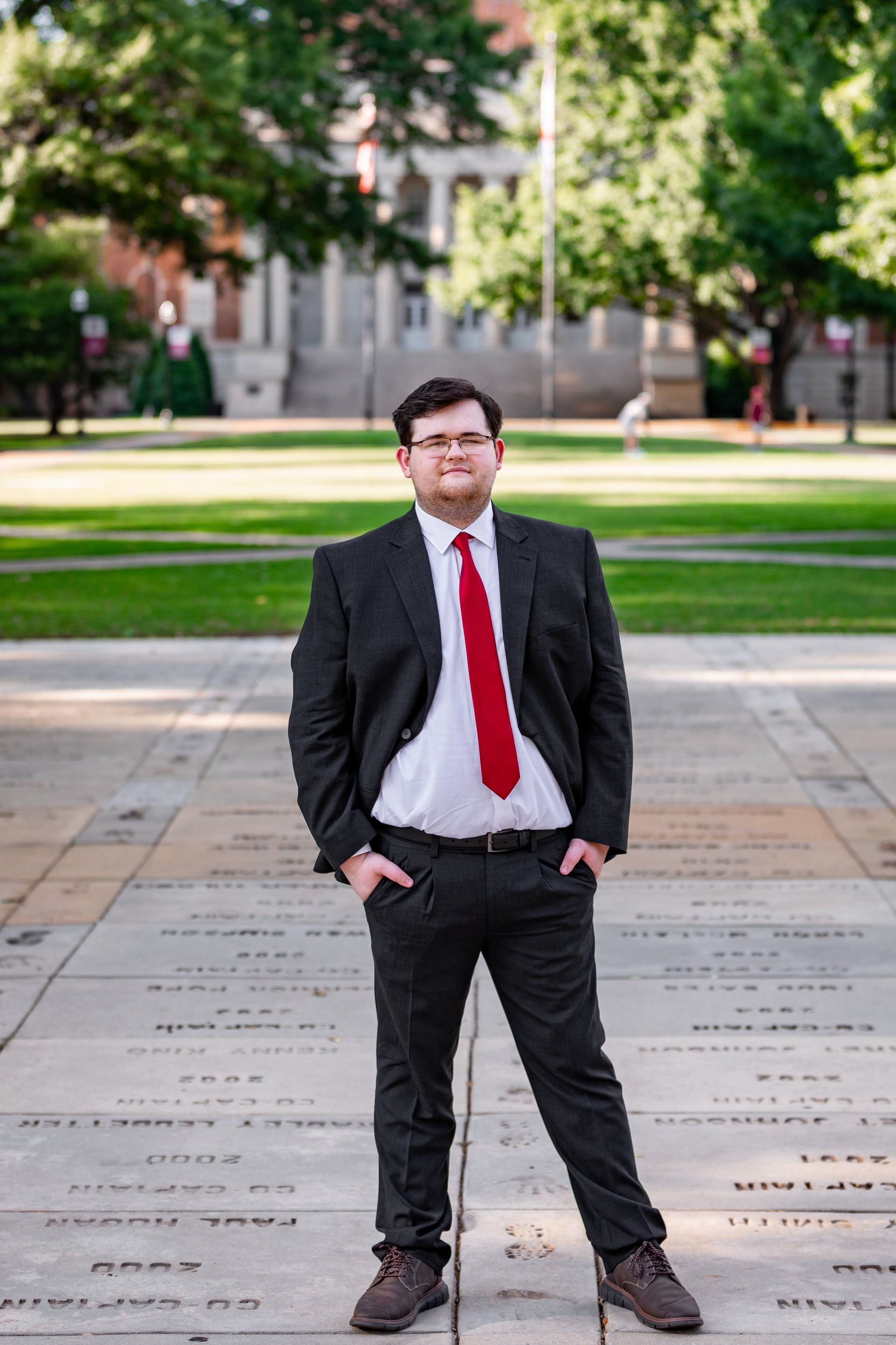 A man in a suit and tie is standing on a sidewalk with his hands in his pockets.