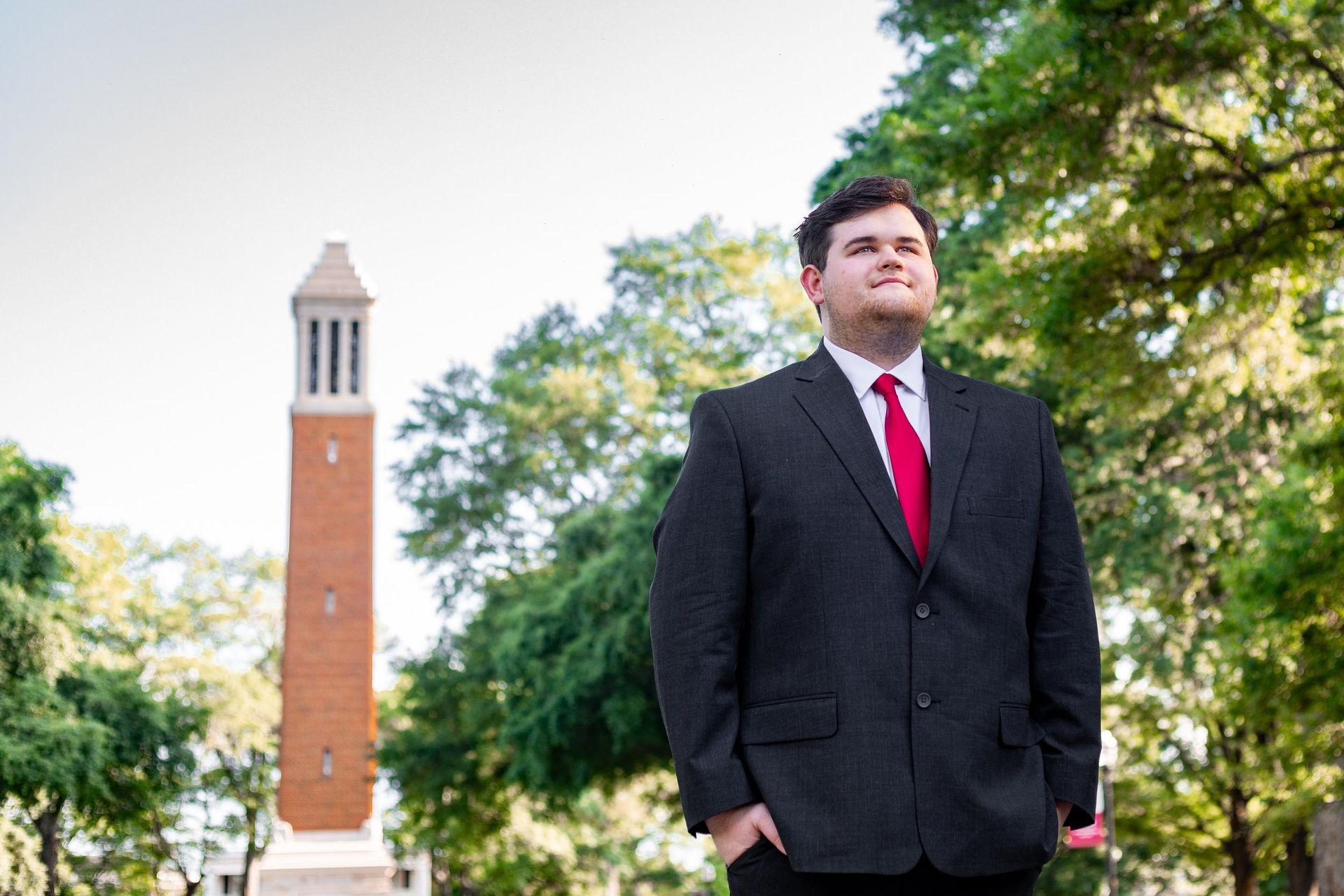 A man in a suit and red tie is standing in front of a bell tower.
