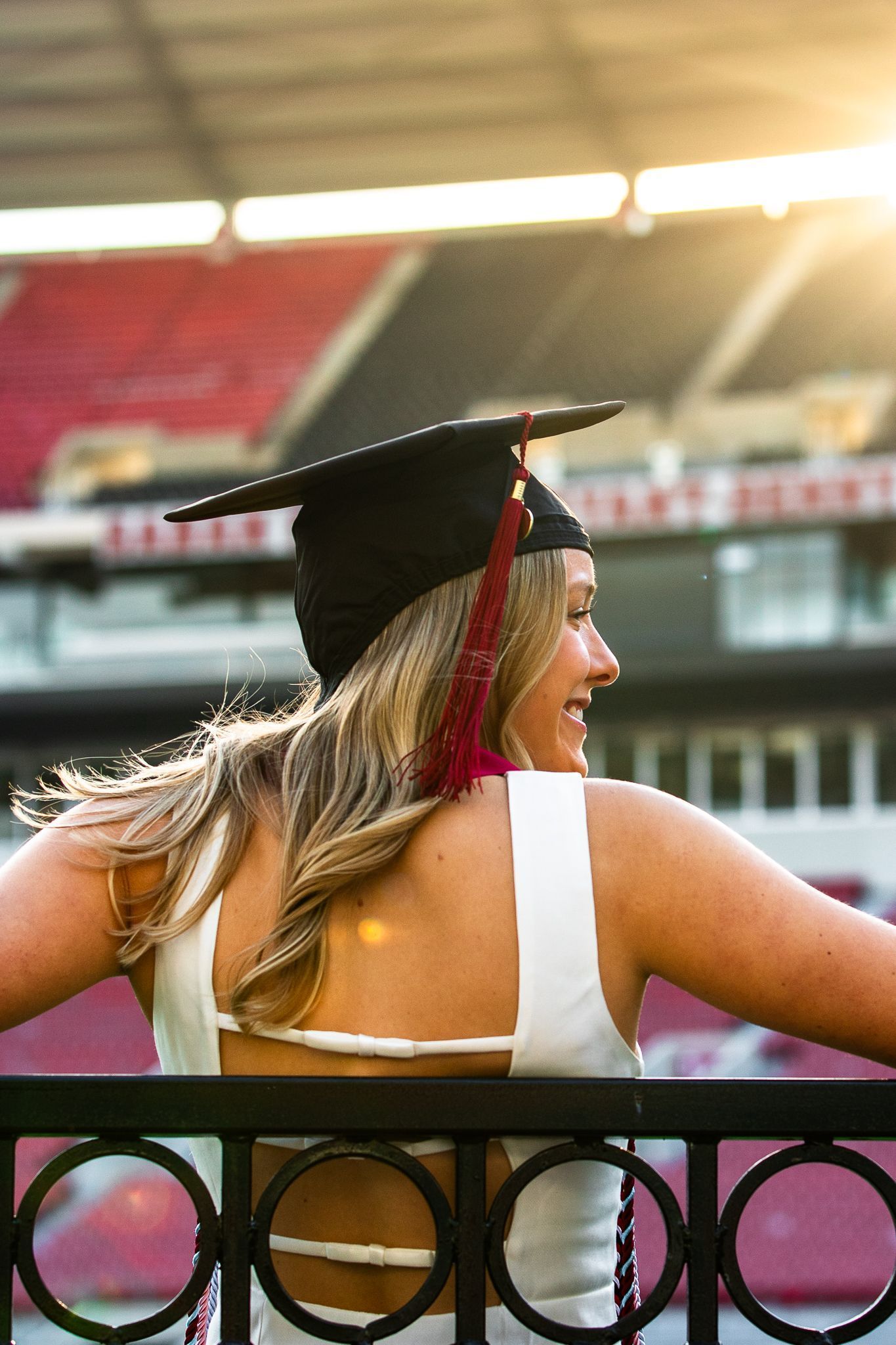 A woman in a graduation cap and gown is standing behind a fence.
