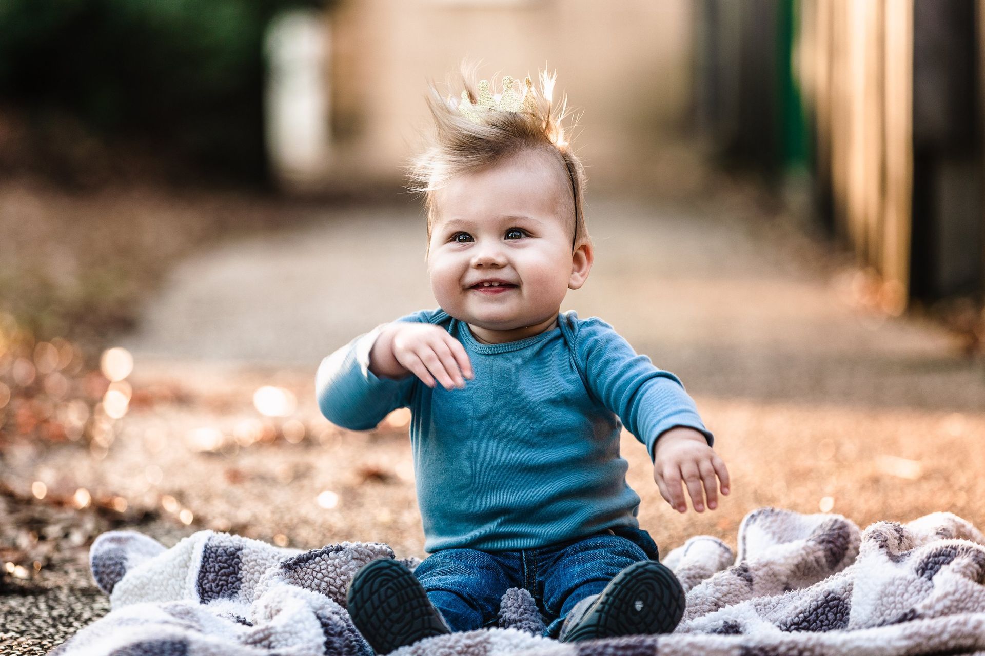 A baby is sitting on a blanket on the ground and smiling.