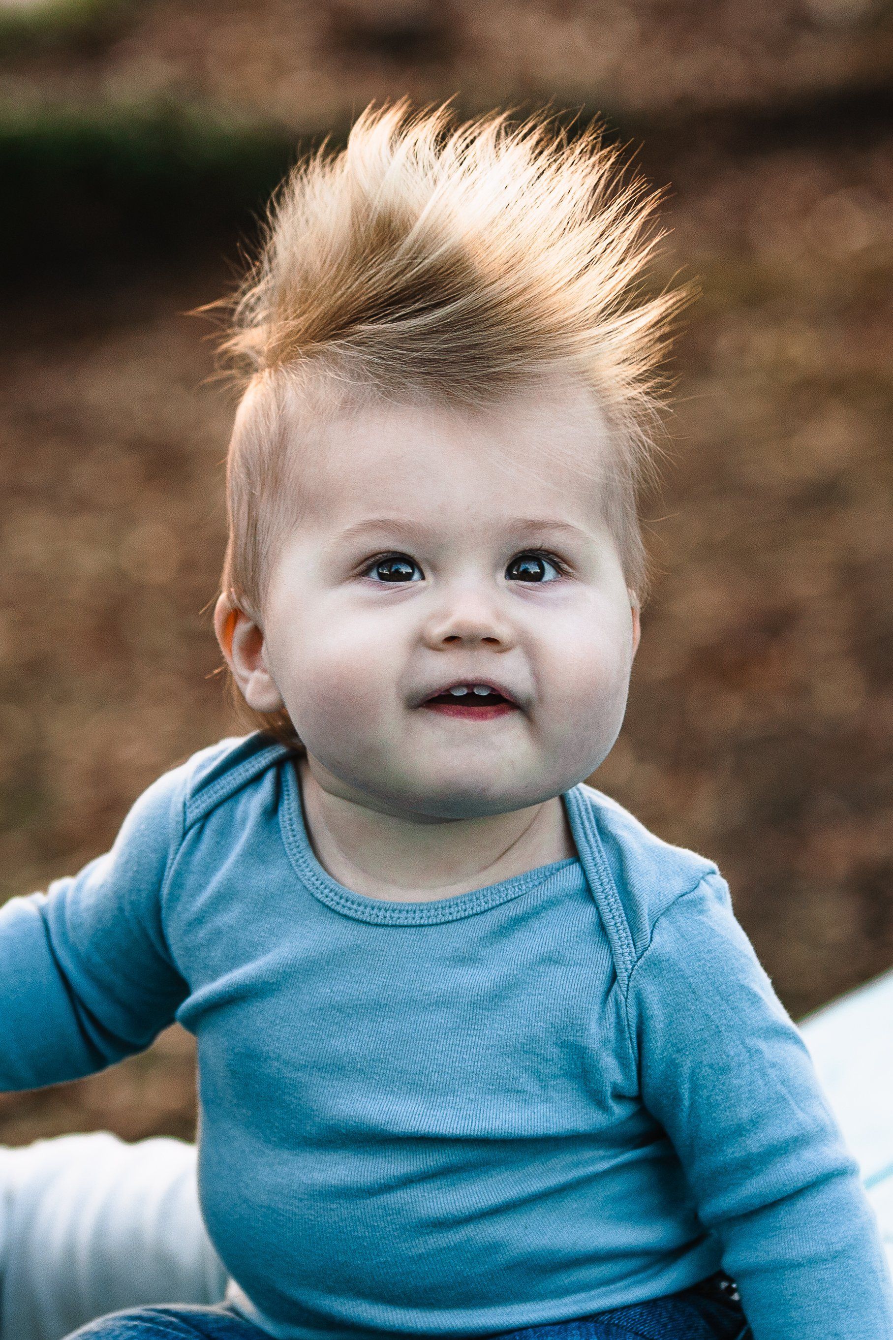 A baby with a mohawk hairstyle is wearing a blue shirt.