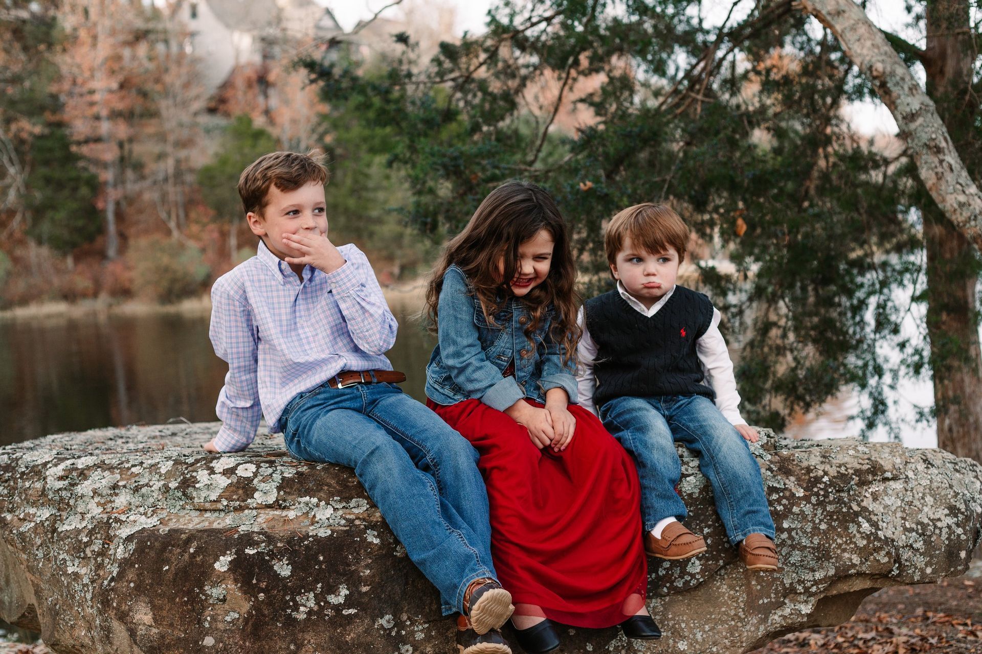 Three children are sitting on a rock near a lake.