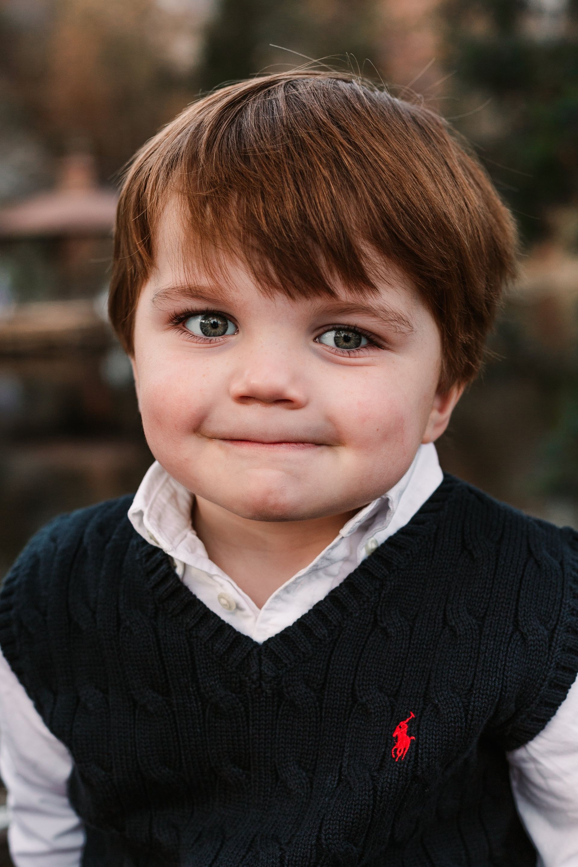 A young boy wearing a black sweater and a white shirt is looking at the camera.