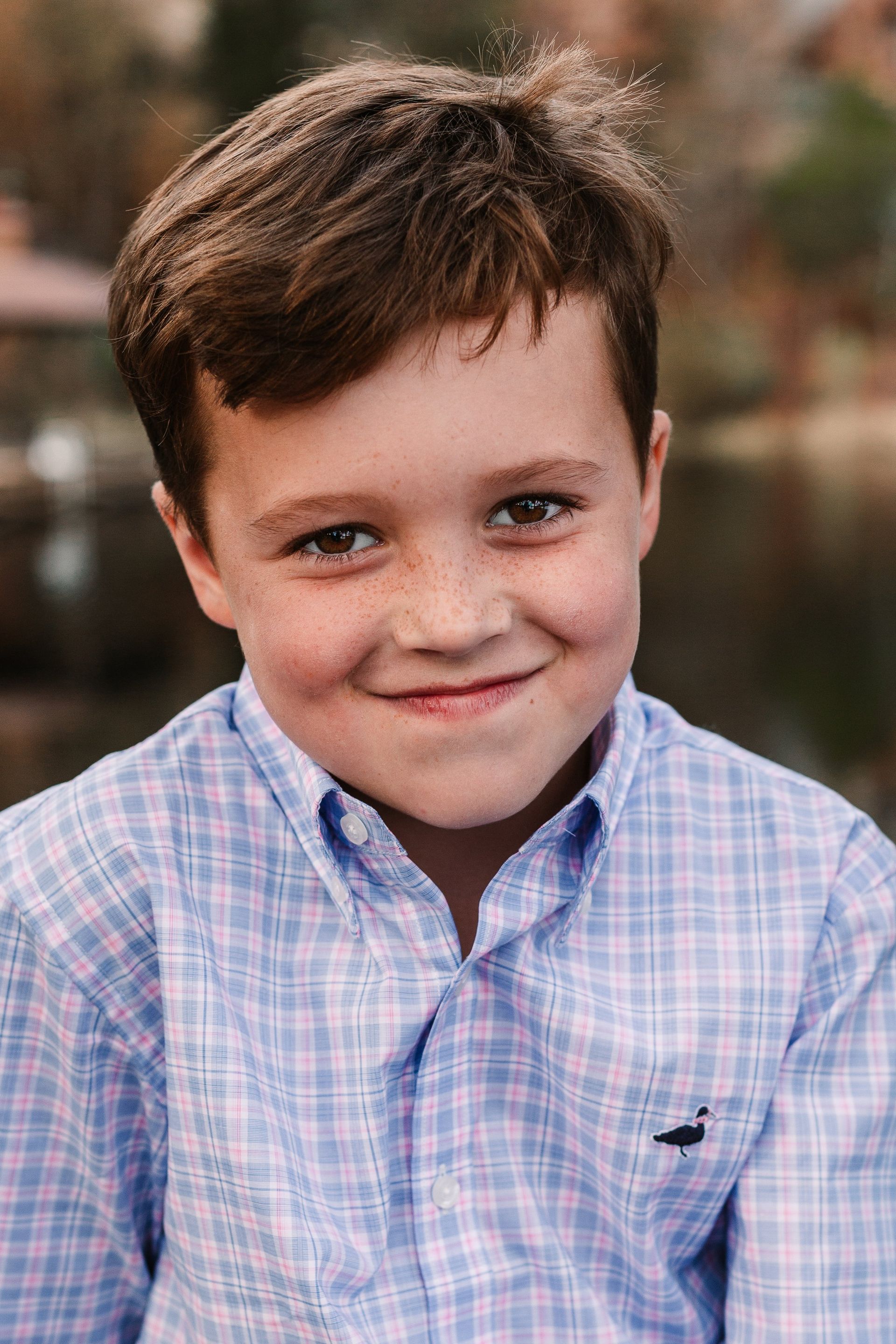 A young boy in a plaid shirt is smiling for the camera.