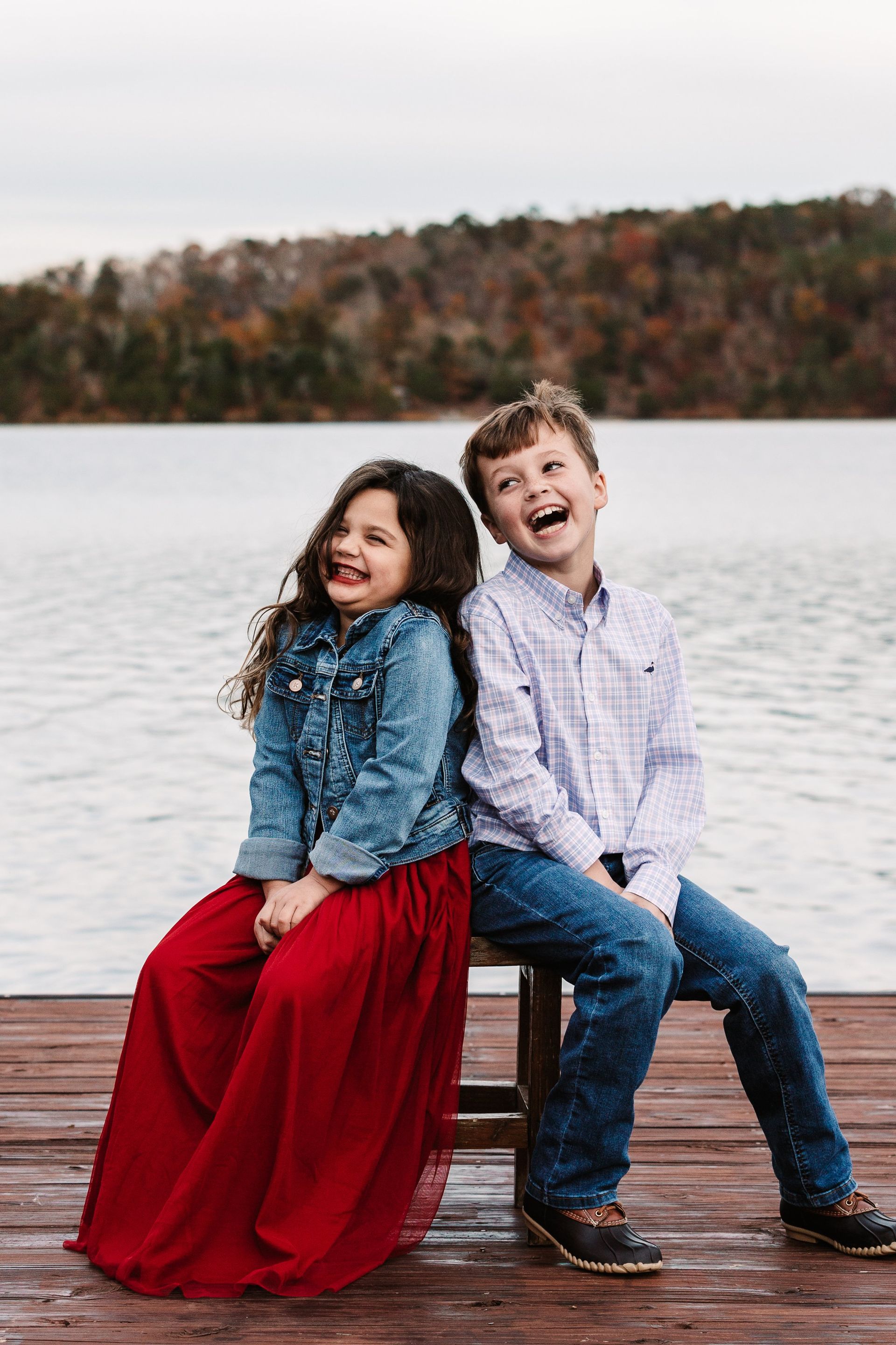 A boy and a girl are sitting back to back on a dock.