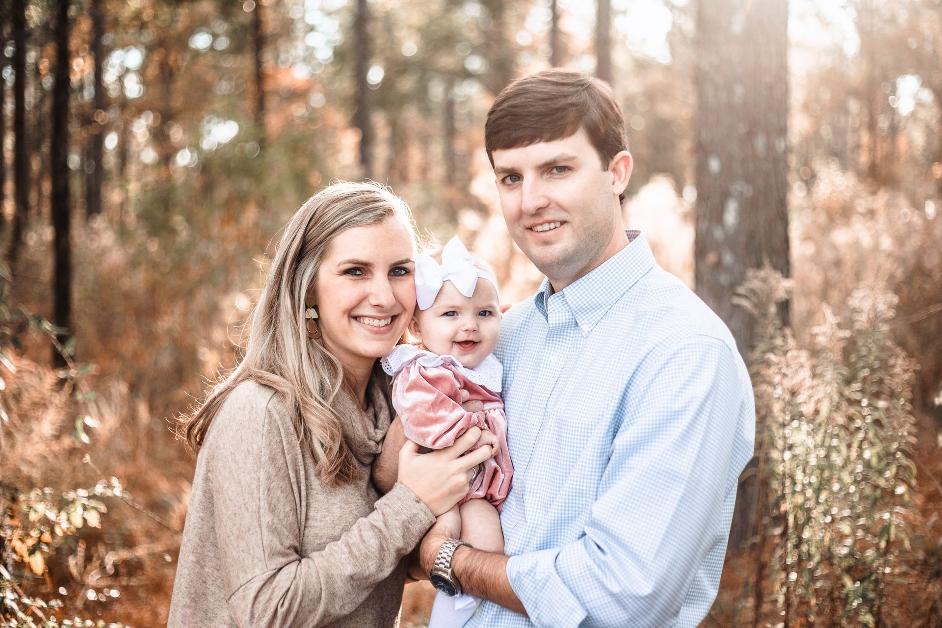 A man and woman are holding a baby in the woods.