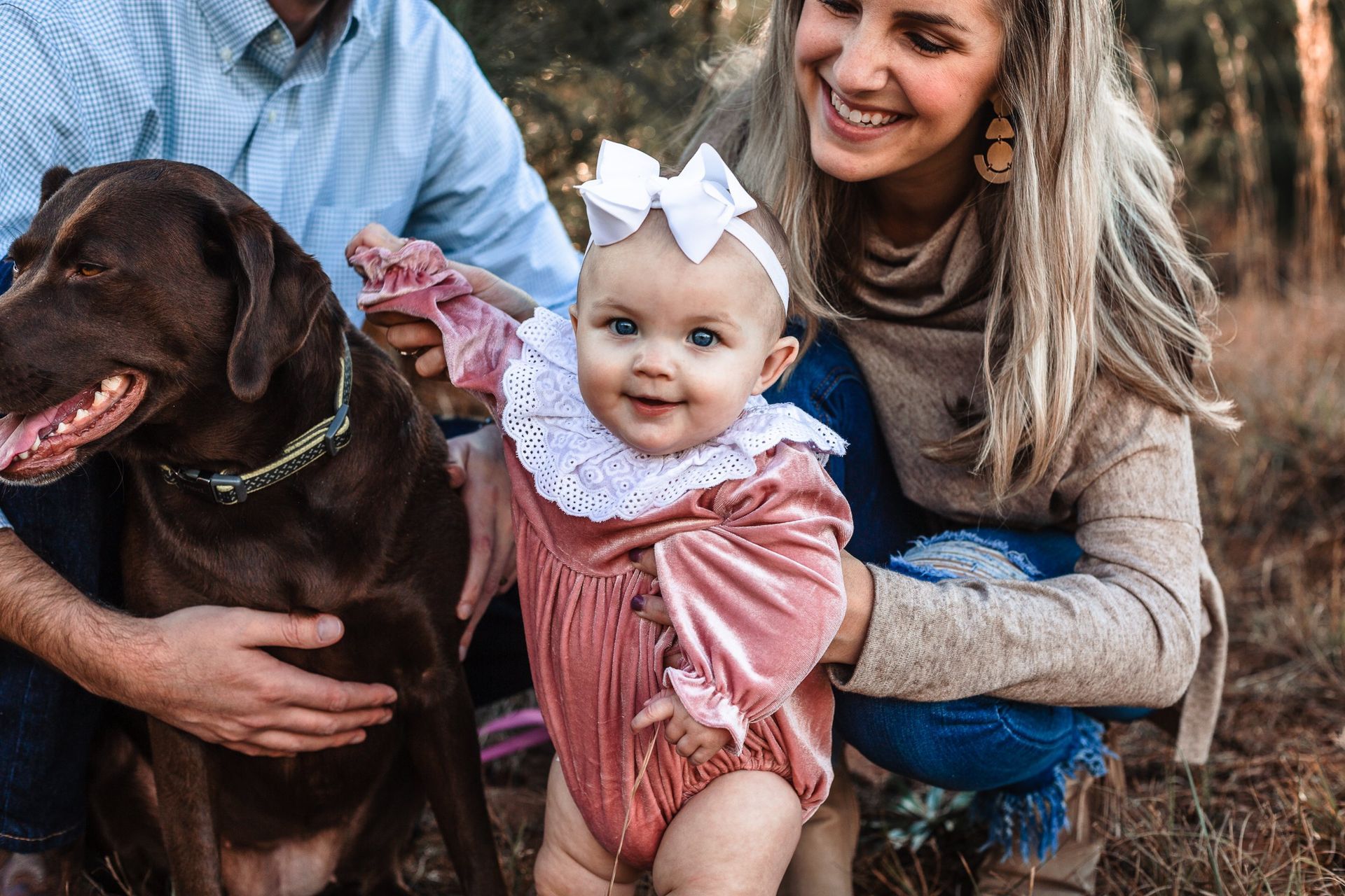 A woman is kneeling down next to a baby and a dog.