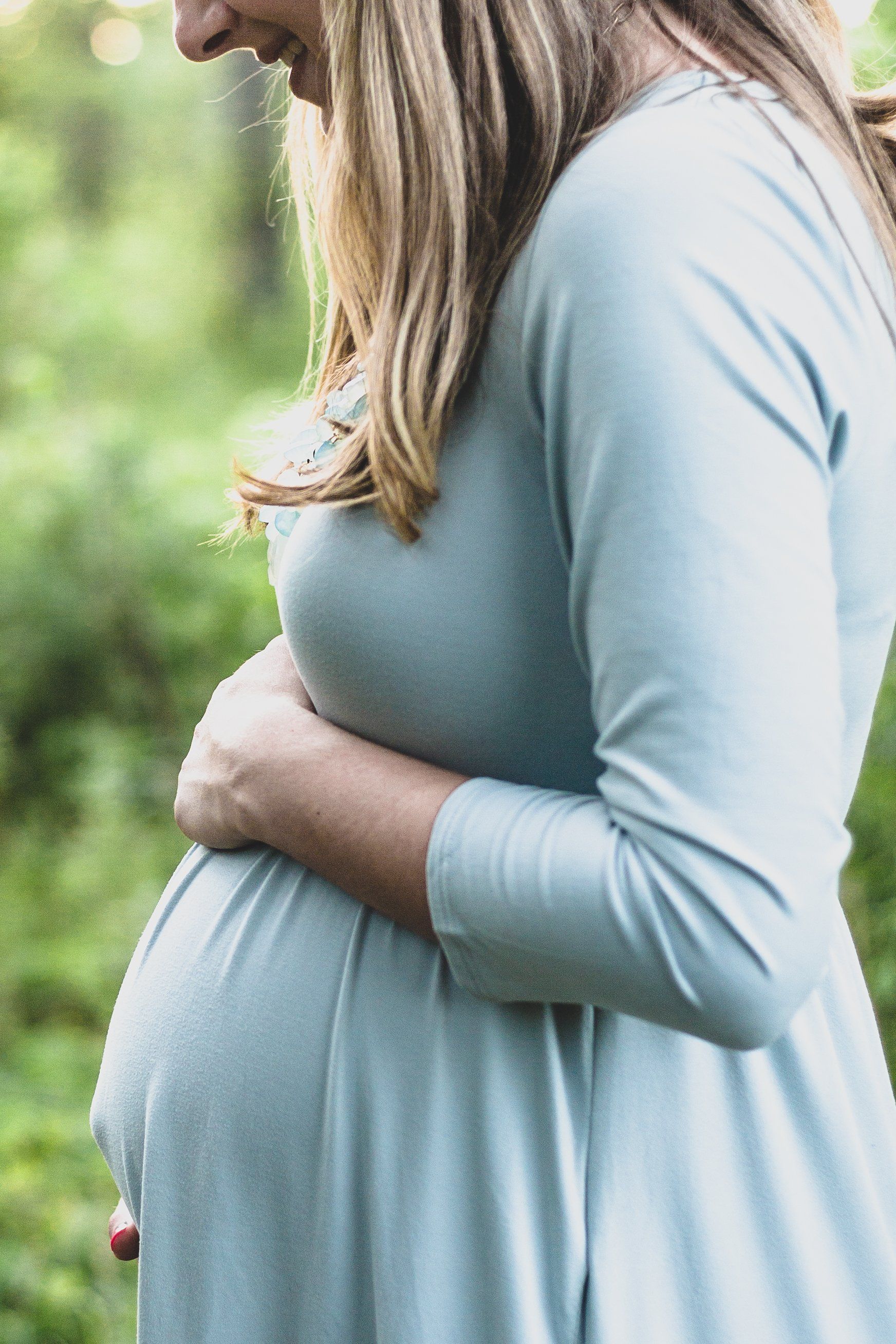 A pregnant woman in a blue dress is holding her belly.