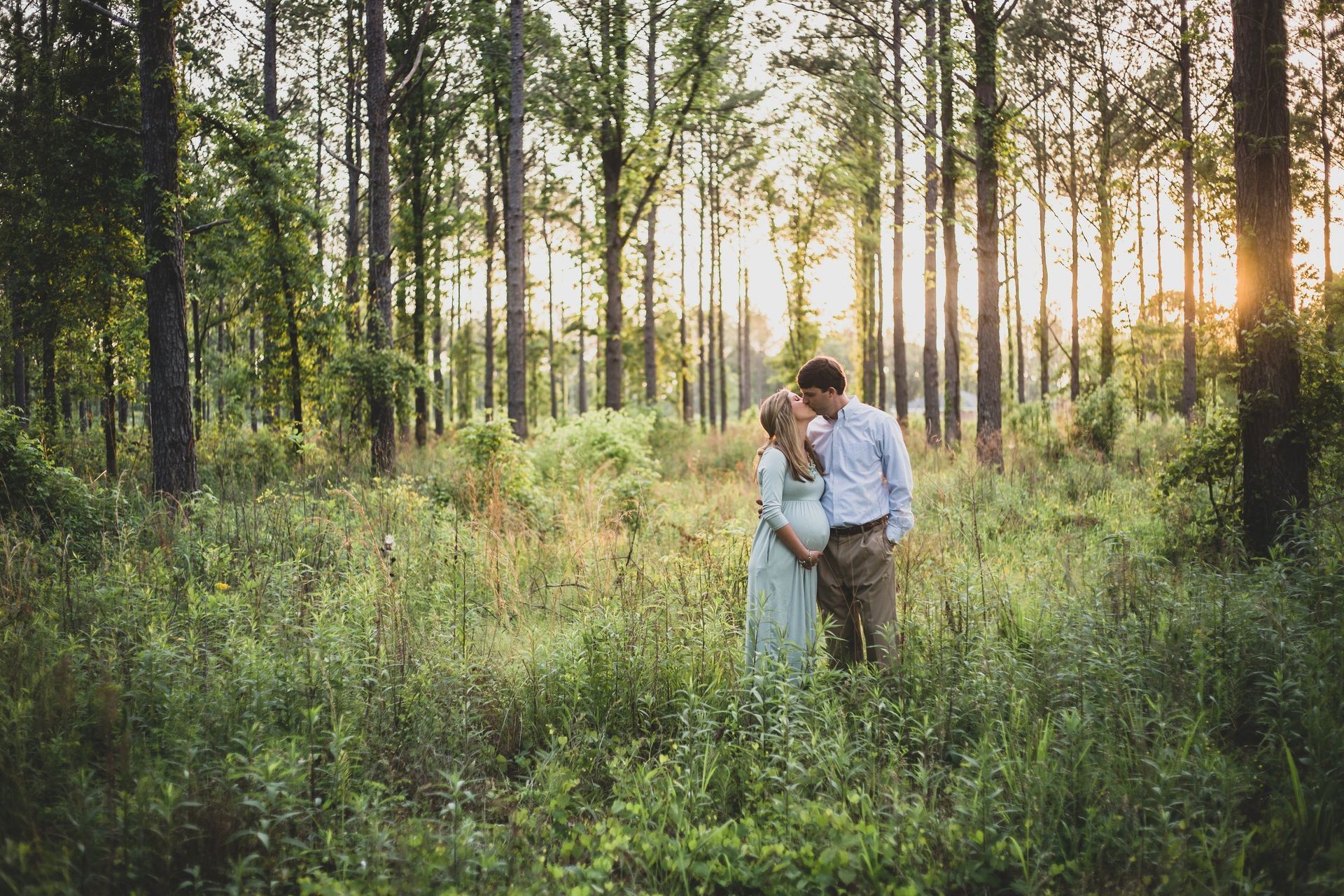 A pregnant woman and a man are standing in the middle of a forest.