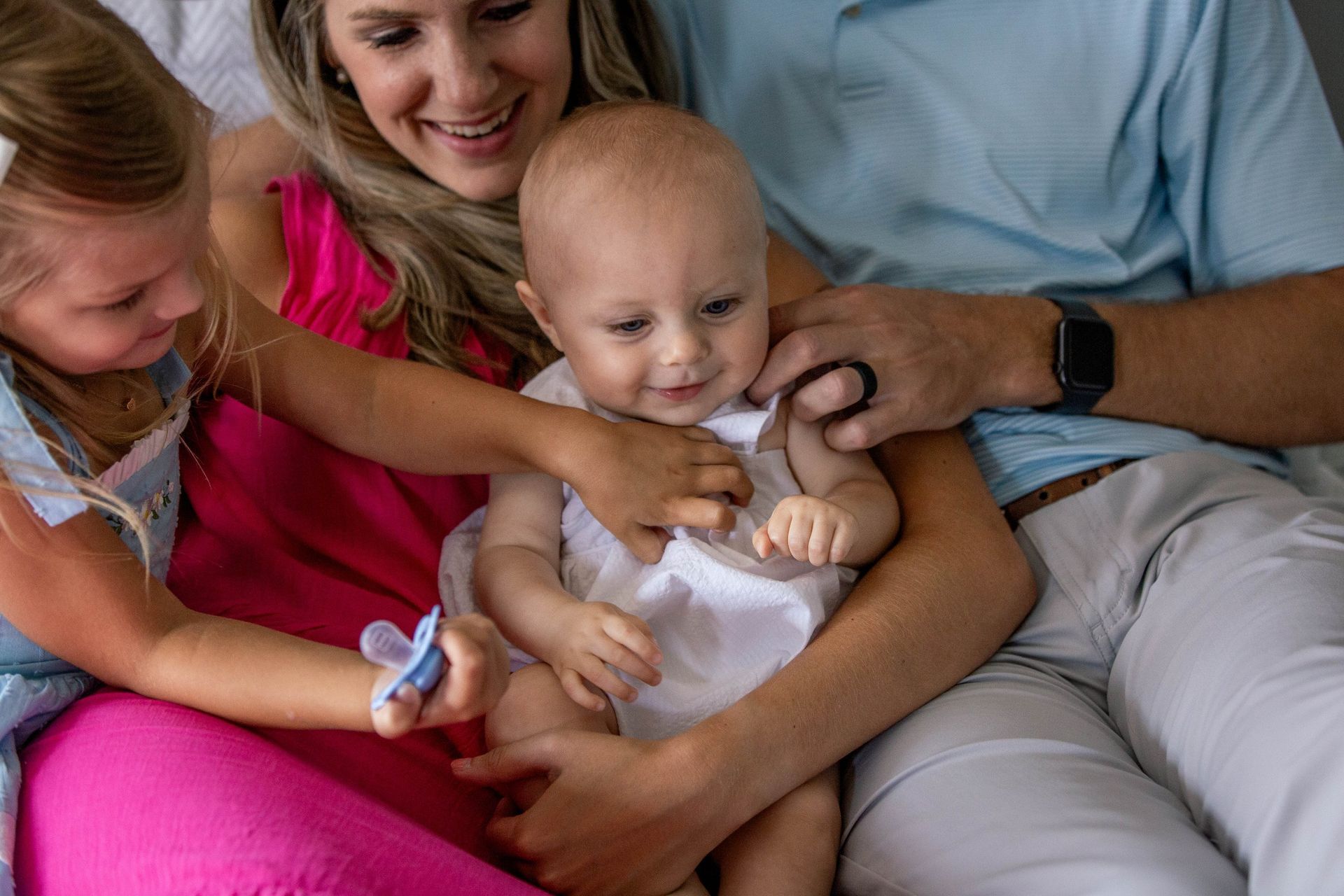 A family is sitting on a couch holding a baby.