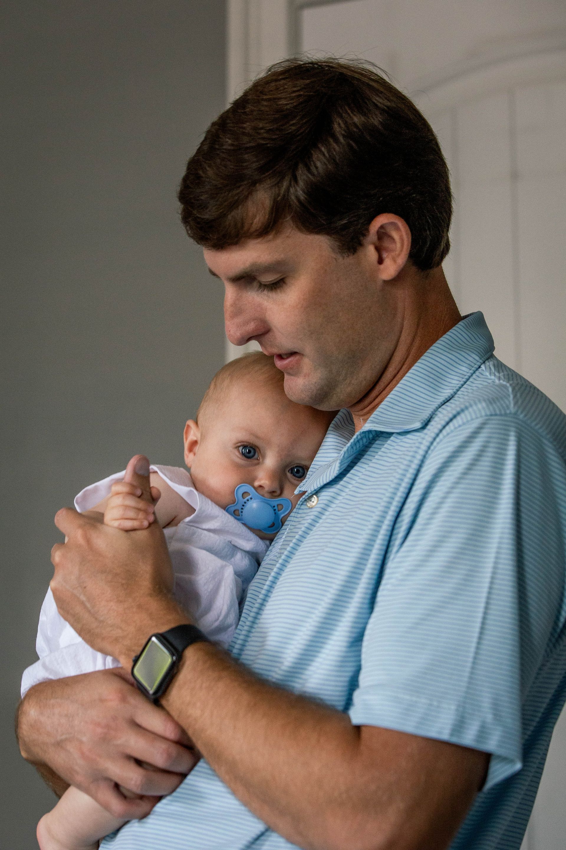 A man is holding a baby with a pacifier in his mouth.