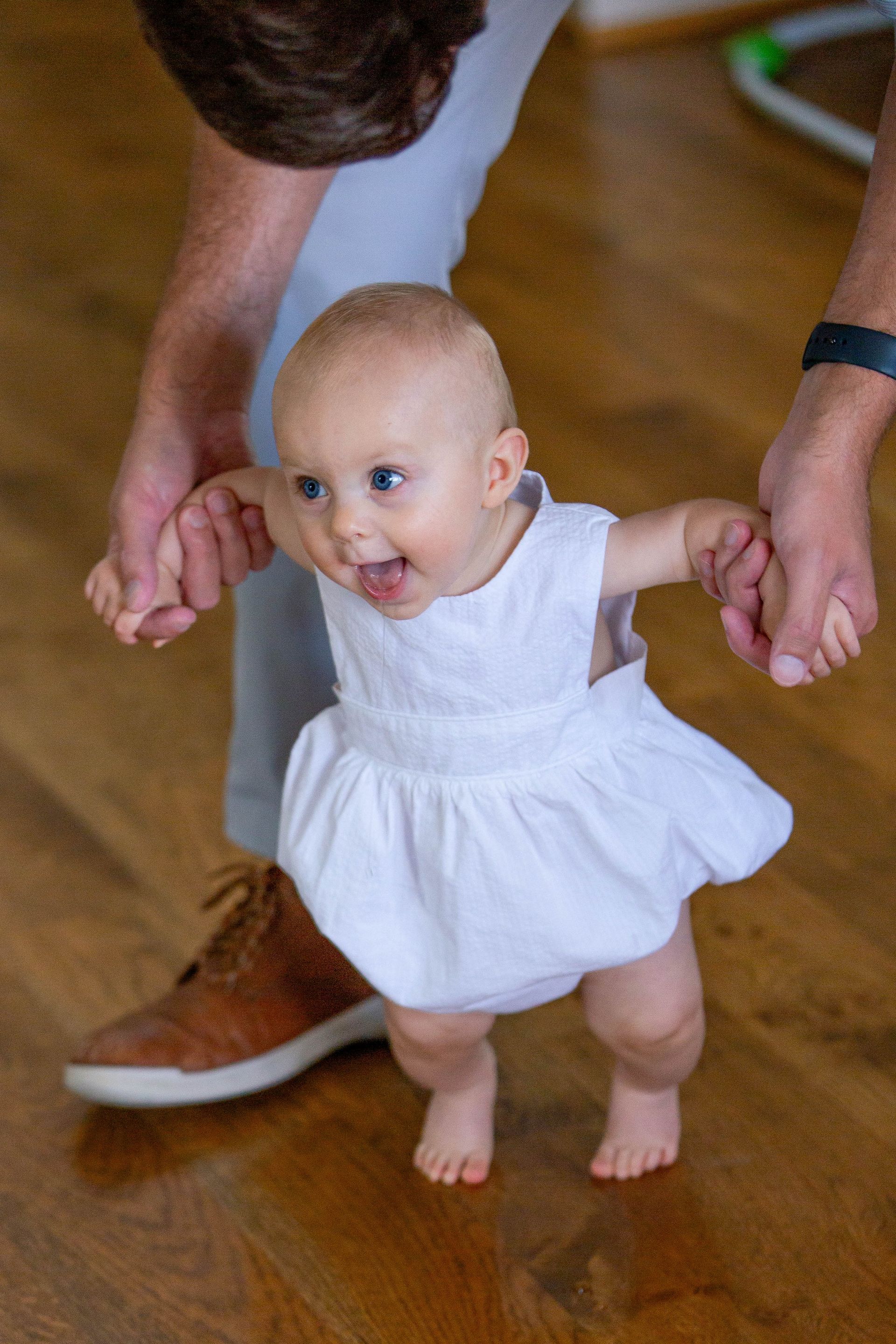 A baby in a white dress is being held by a man.