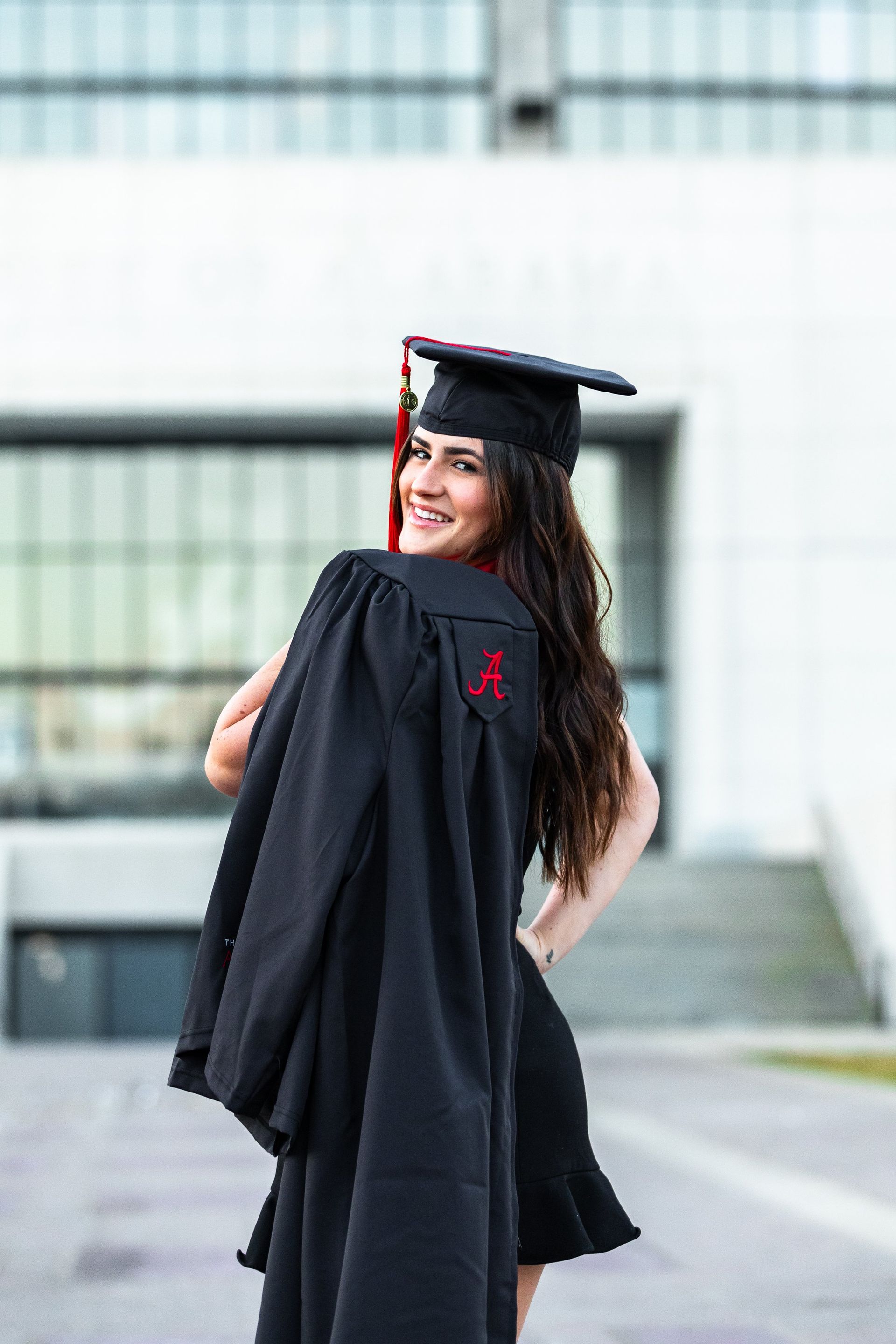 A woman in a graduation cap and gown is standing in front of a building.