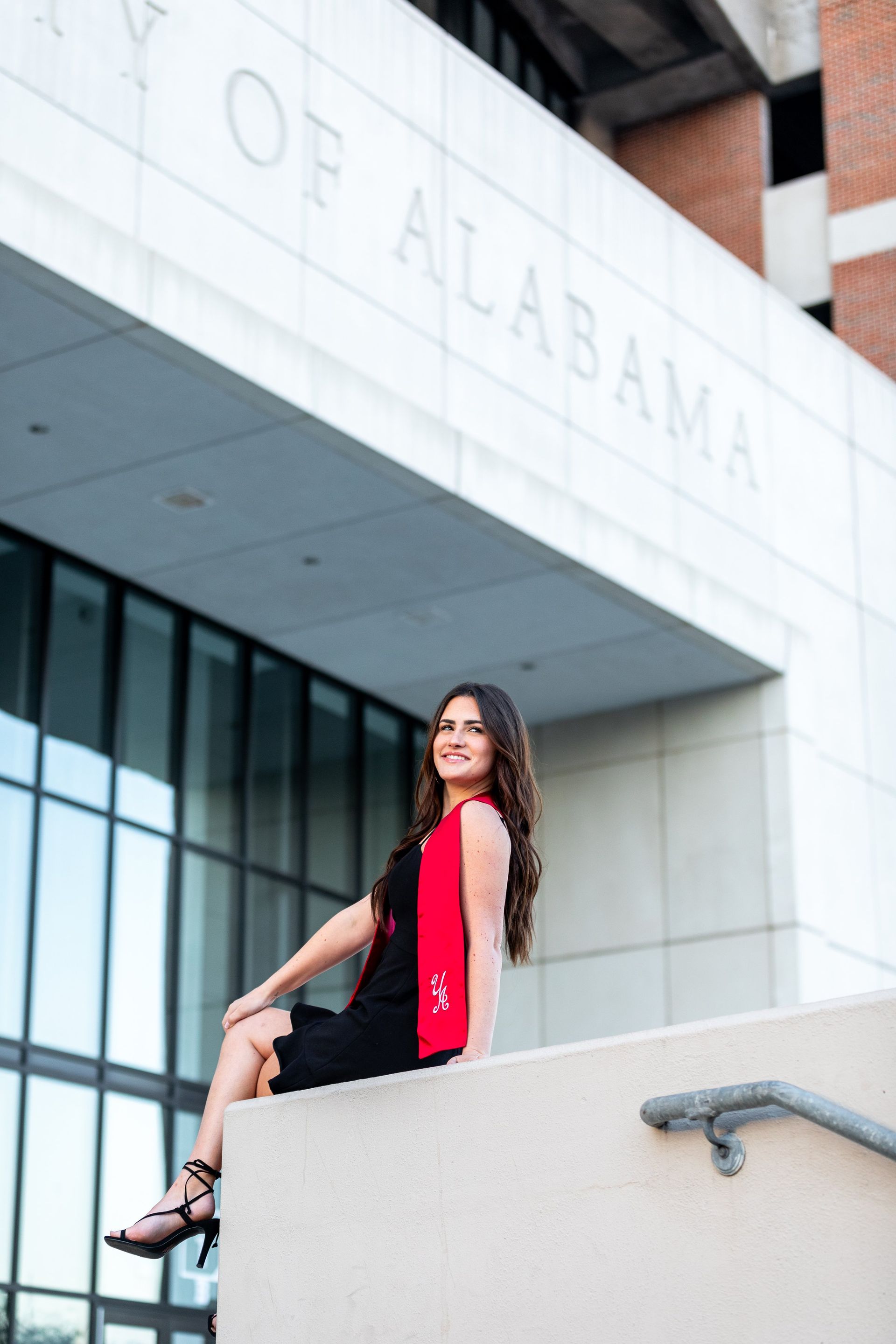 A woman is sitting on a wall in front of a building that says city of alabama