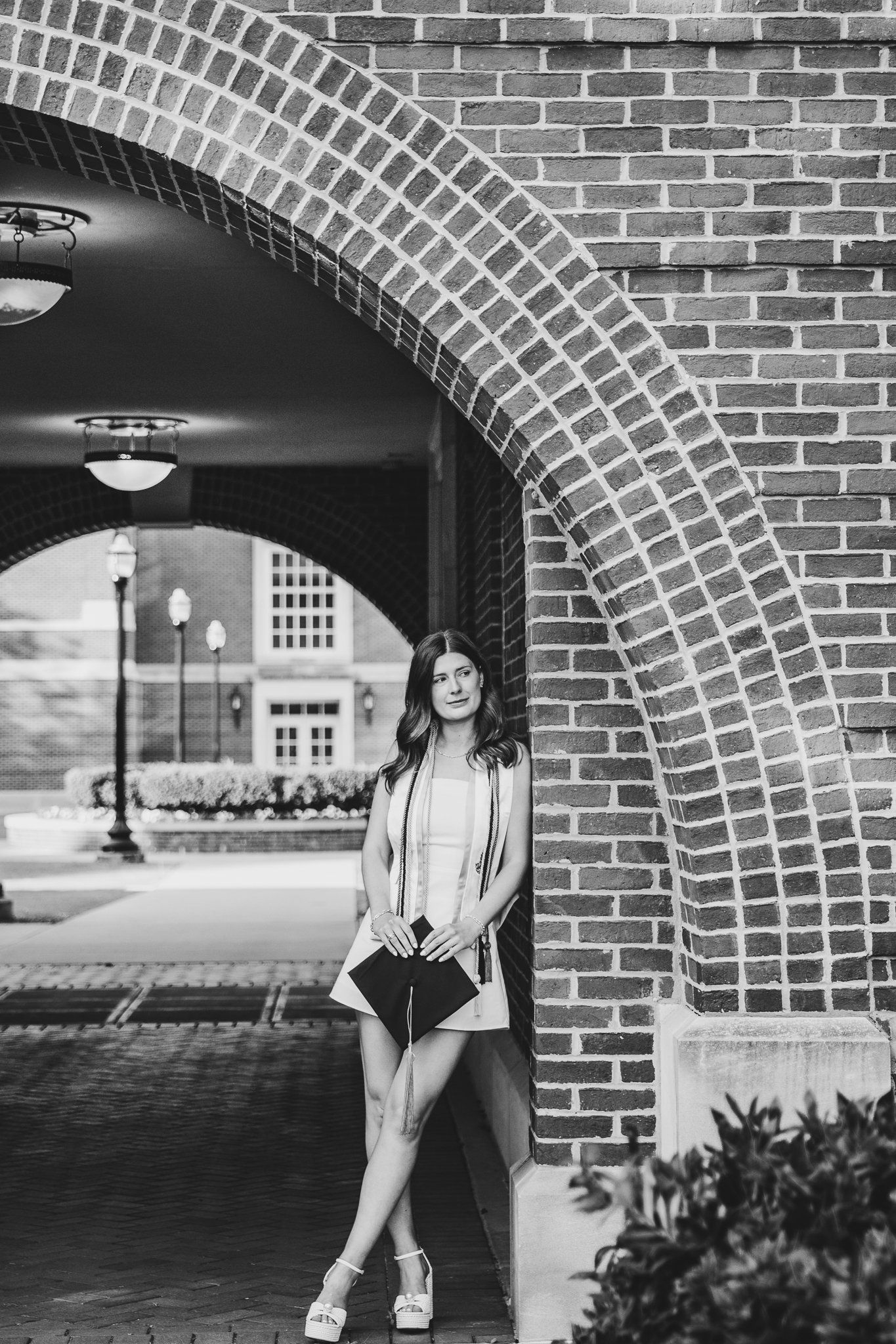 A black and white photo of a woman standing in front of a brick archway.